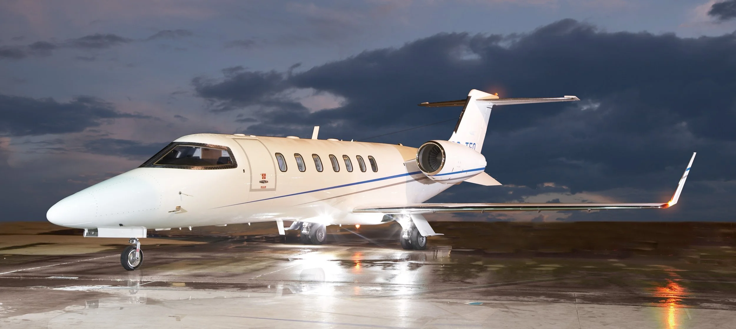 Private jet airplane on the tarmac at dusk with dark cloudy sky in the background.