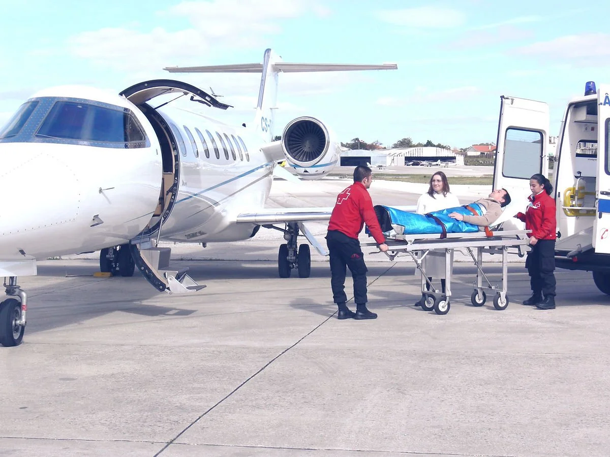 Medical personnel loading a patient on a gurney into a private jet at an airport.