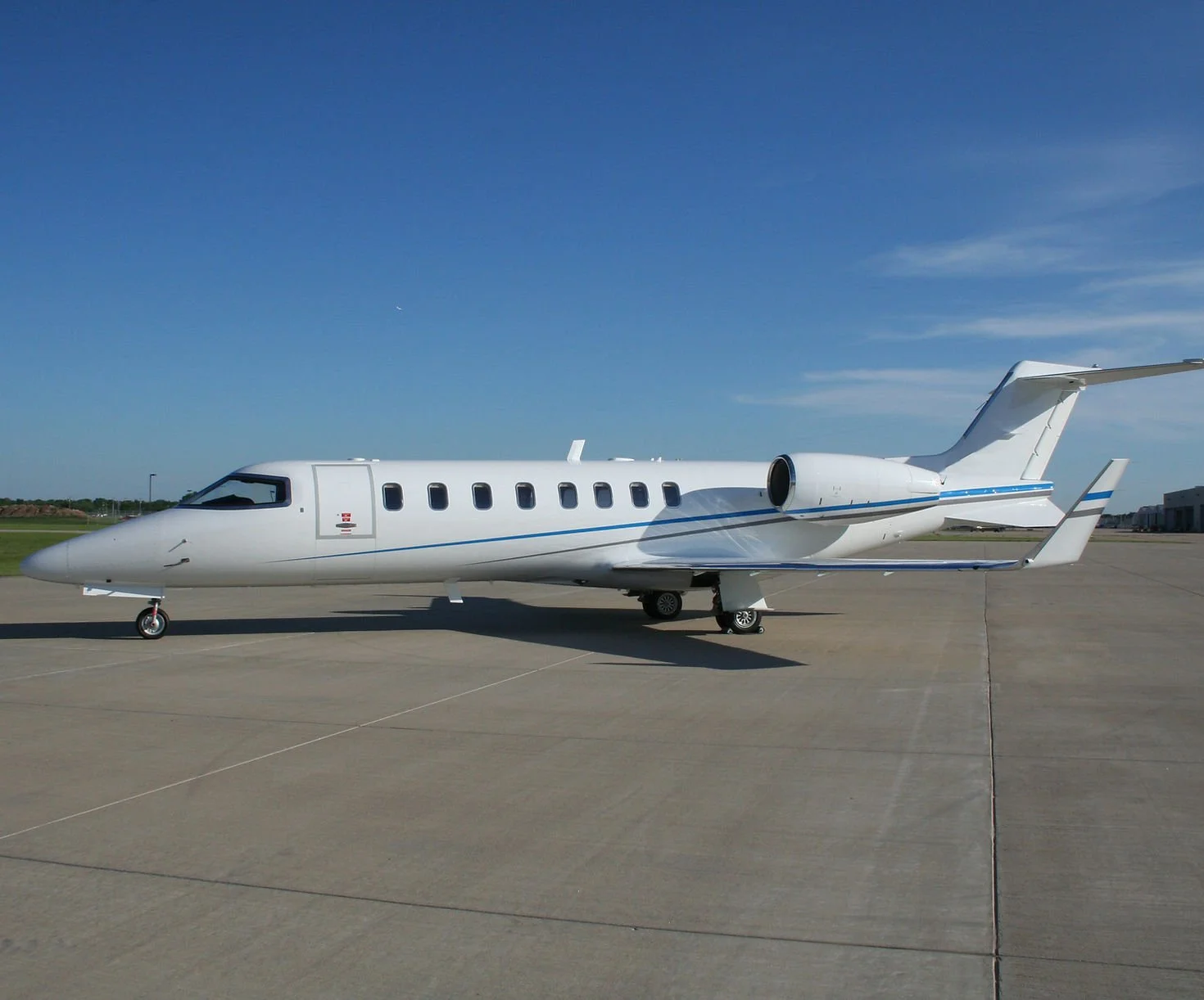 White private jet airplane parked on tarmac under clear blue sky