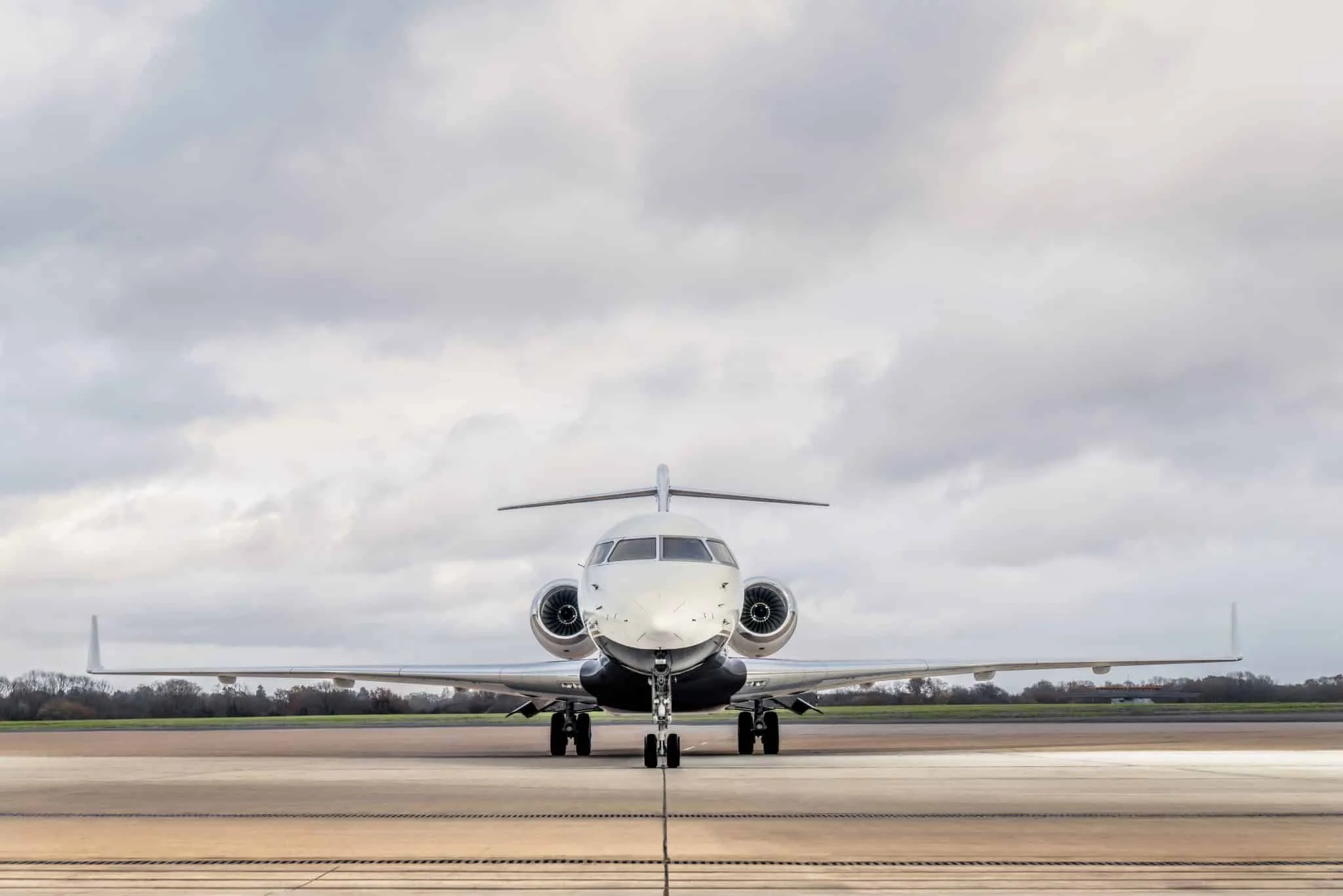 Front view of a private jet airplane parked on an airport tarmac under a cloudy sky.