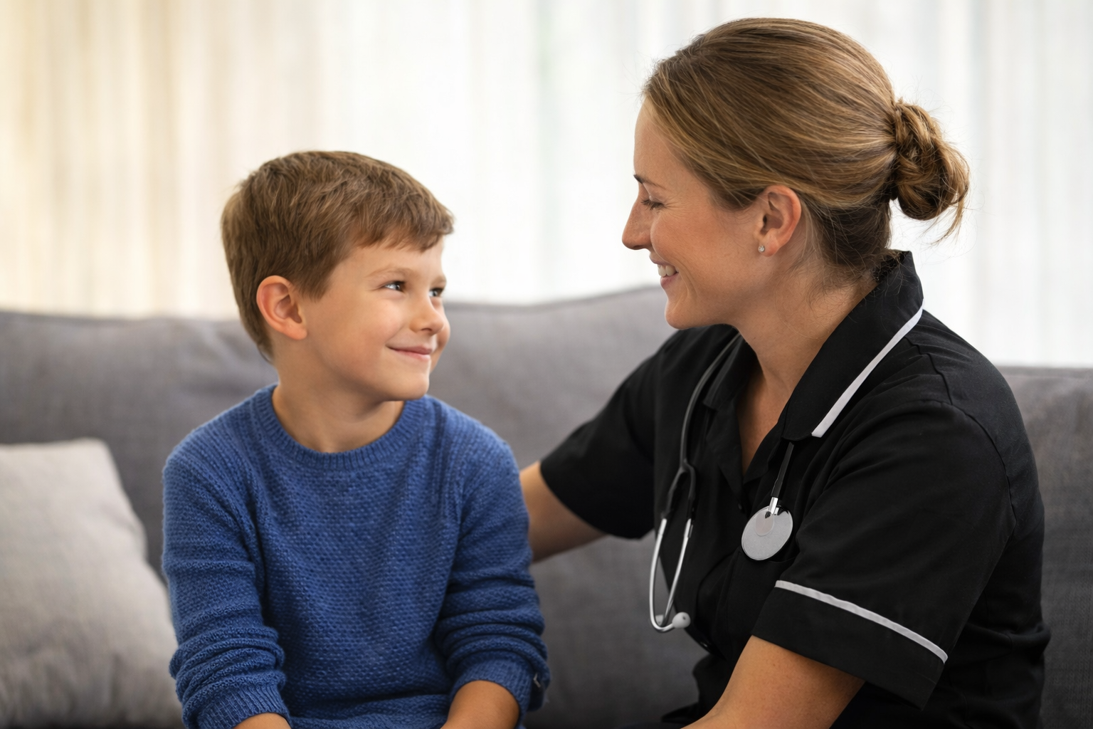 A young boy and a female nurse or doctor smiling at each other in a clinical setting.