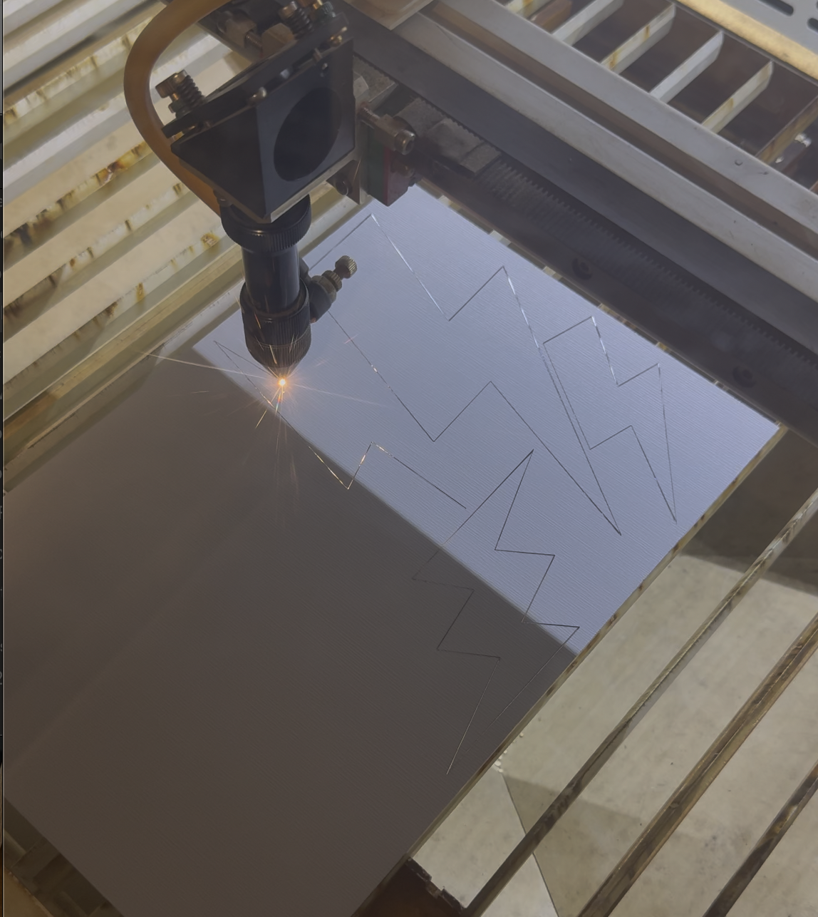 A laser cutter engraving a geometric star design onto a metal sheet.