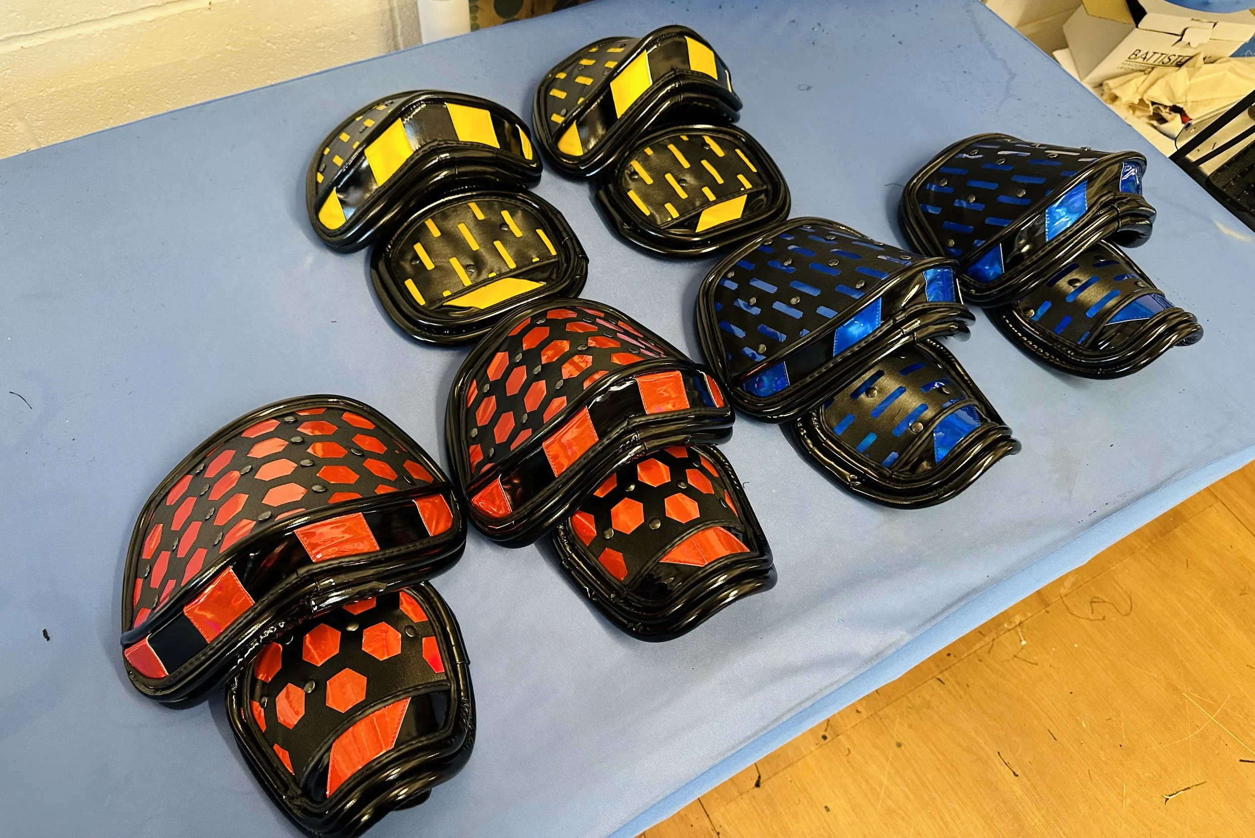 Colorful protective shoulder armour with geometric patterns in red, yellow, and blue, arranged on a blue surface. trucks from starlight express, troubadour Wembley. 