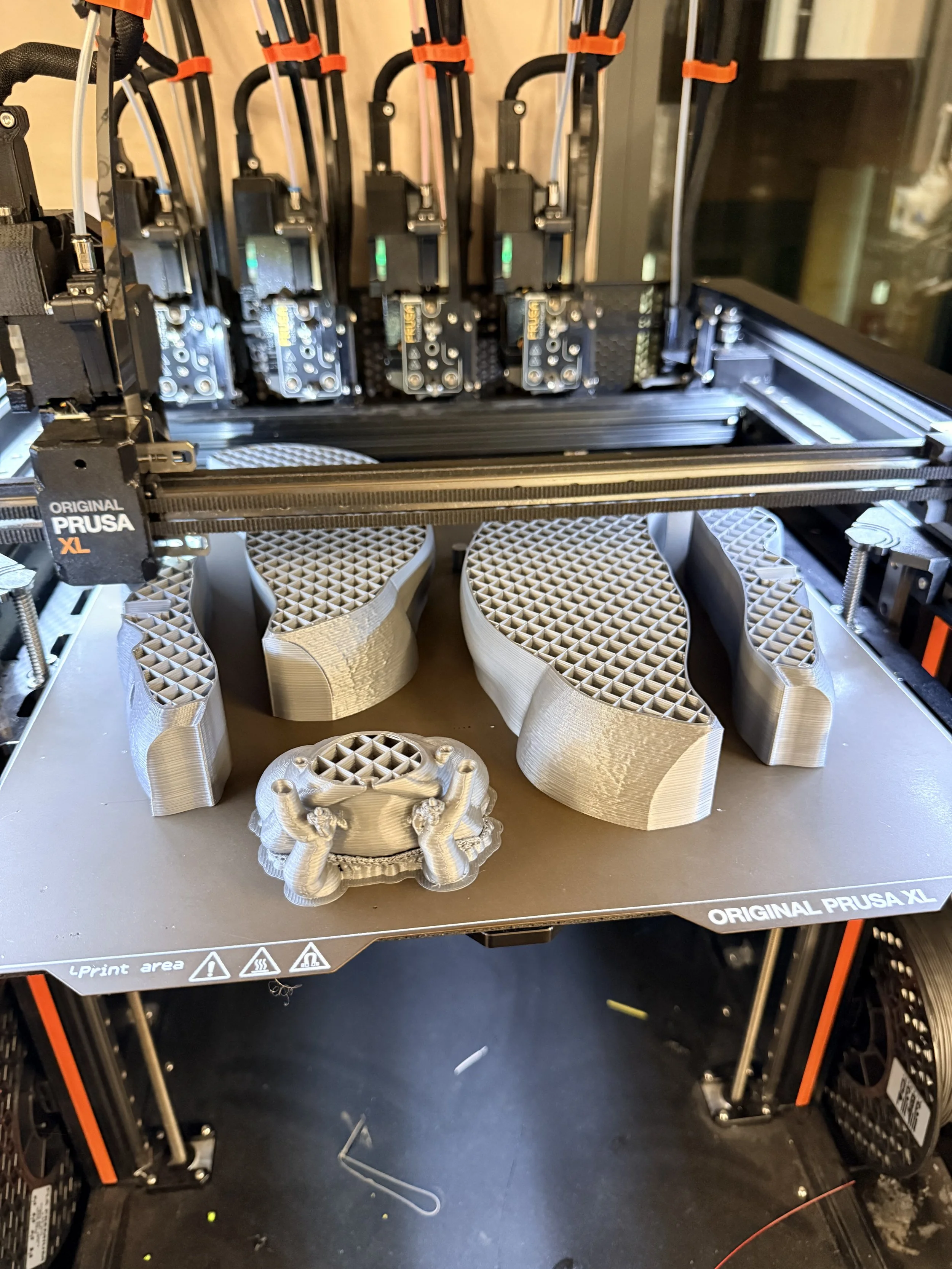 3D-printed objects on a 3D printer bed, with intricate lattice structures, in various shapes and sizes.