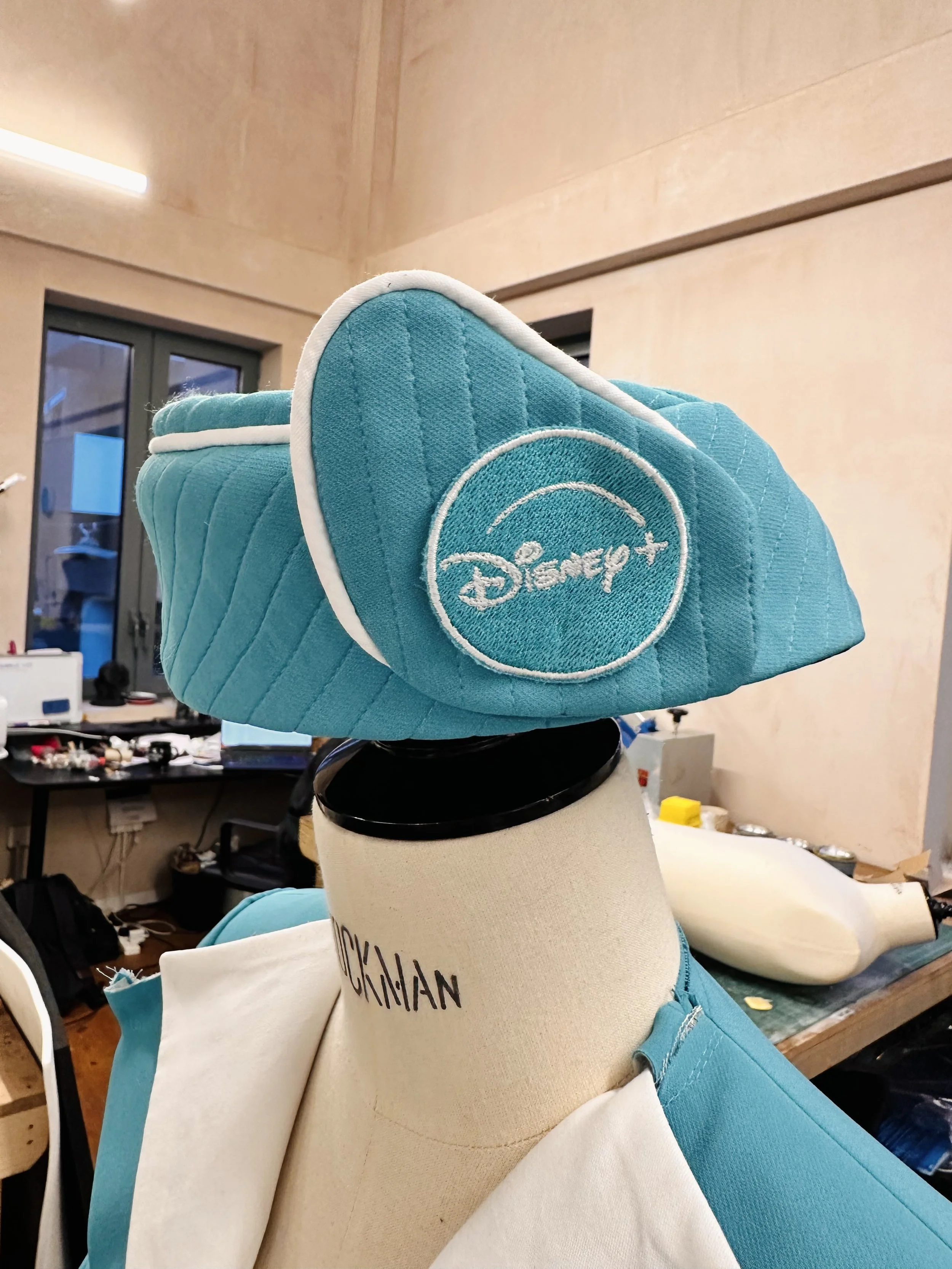 A teal quilted Disney+ cap on a mannequin head in a workshop.