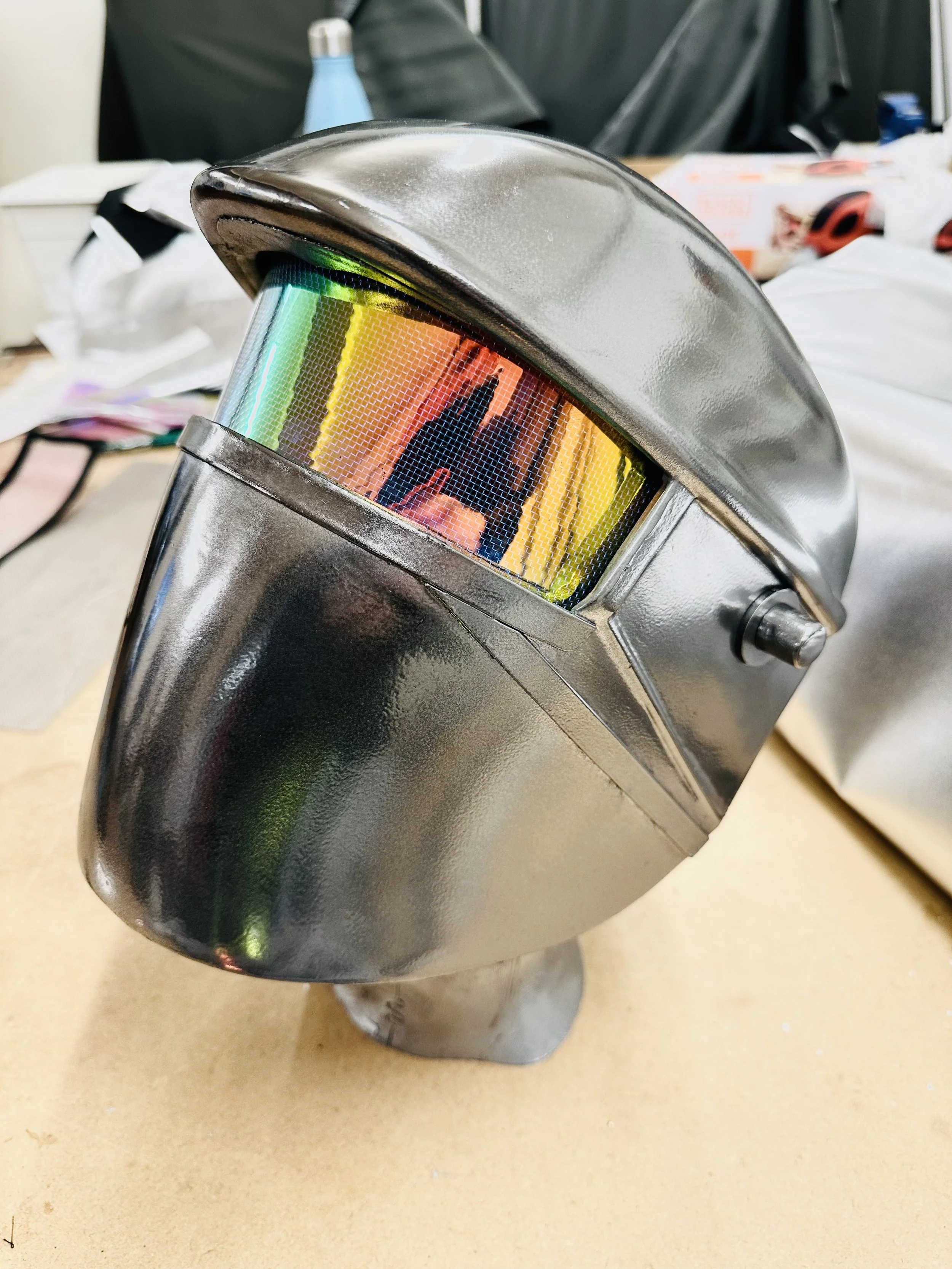A welding helmet with a reflective, rainbow-colored visor placed on a table.