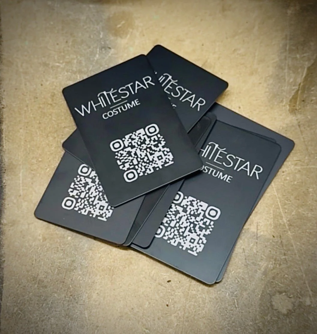 Multiple black cards with the text 'WHITE STAR COSTUME' and a QR code on each, placed on a wooden surface.