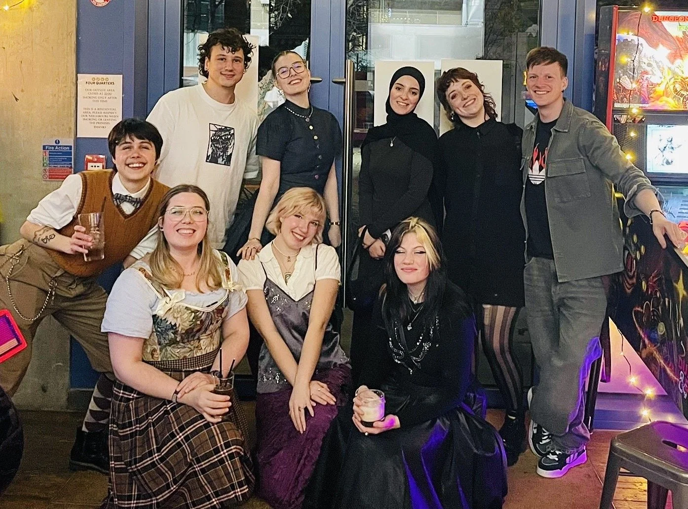 A group of ten young adults posing together in a bar or club, some holding drinks, smiling and enjoying the moment. The collaborative Whitestar costume making team enjoying their Christmas night out.