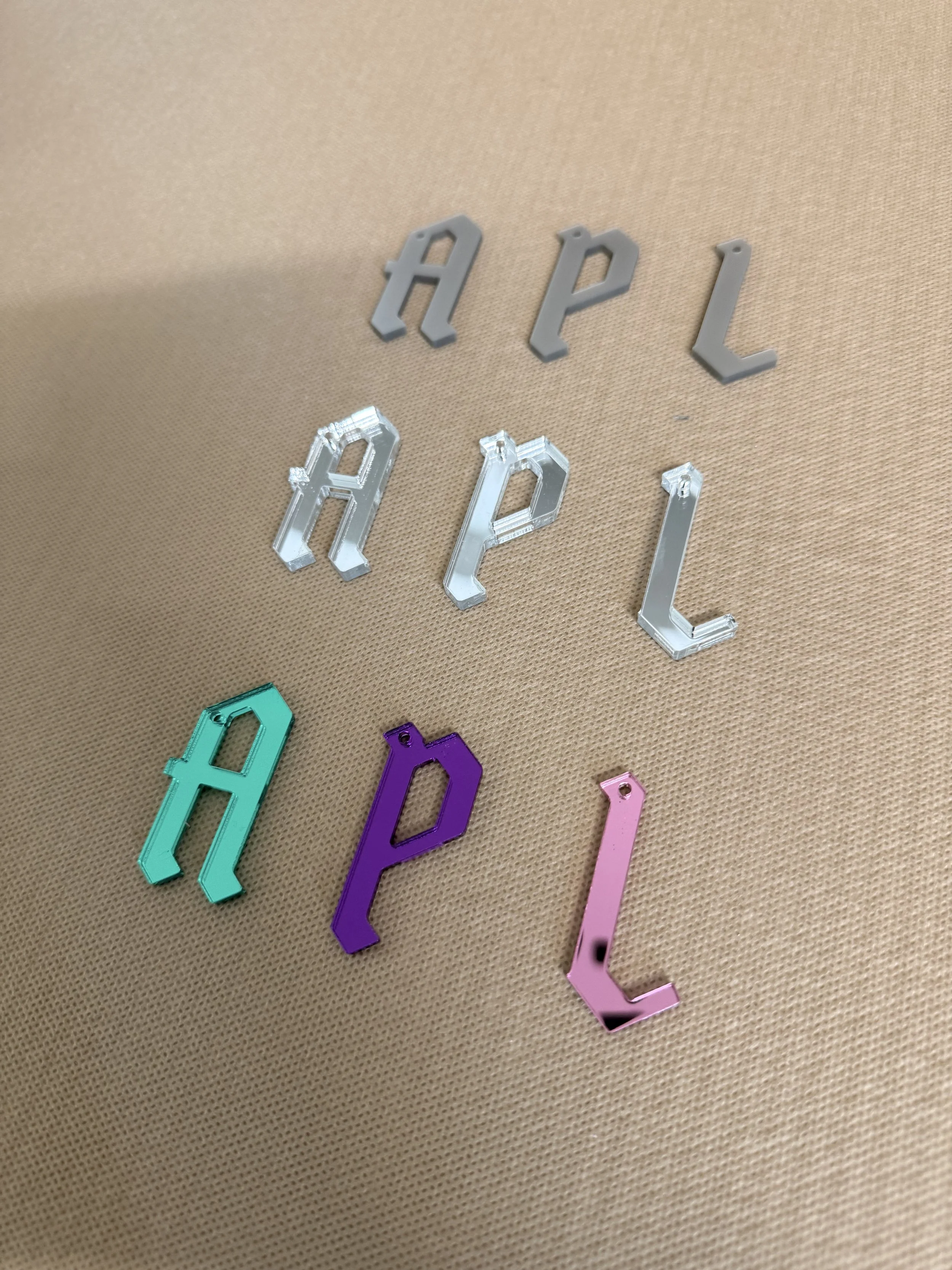 Colorful plastic letter charms spelling out the word 'APRIL' on a beige textured surface.
