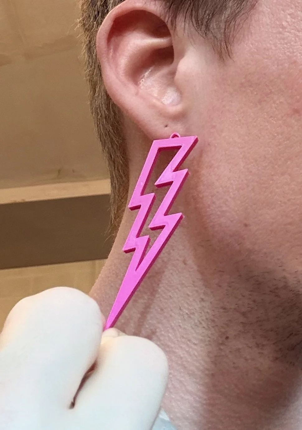Person wearing a large pink lightning bolt-shaped earring, close-up of ear and face.