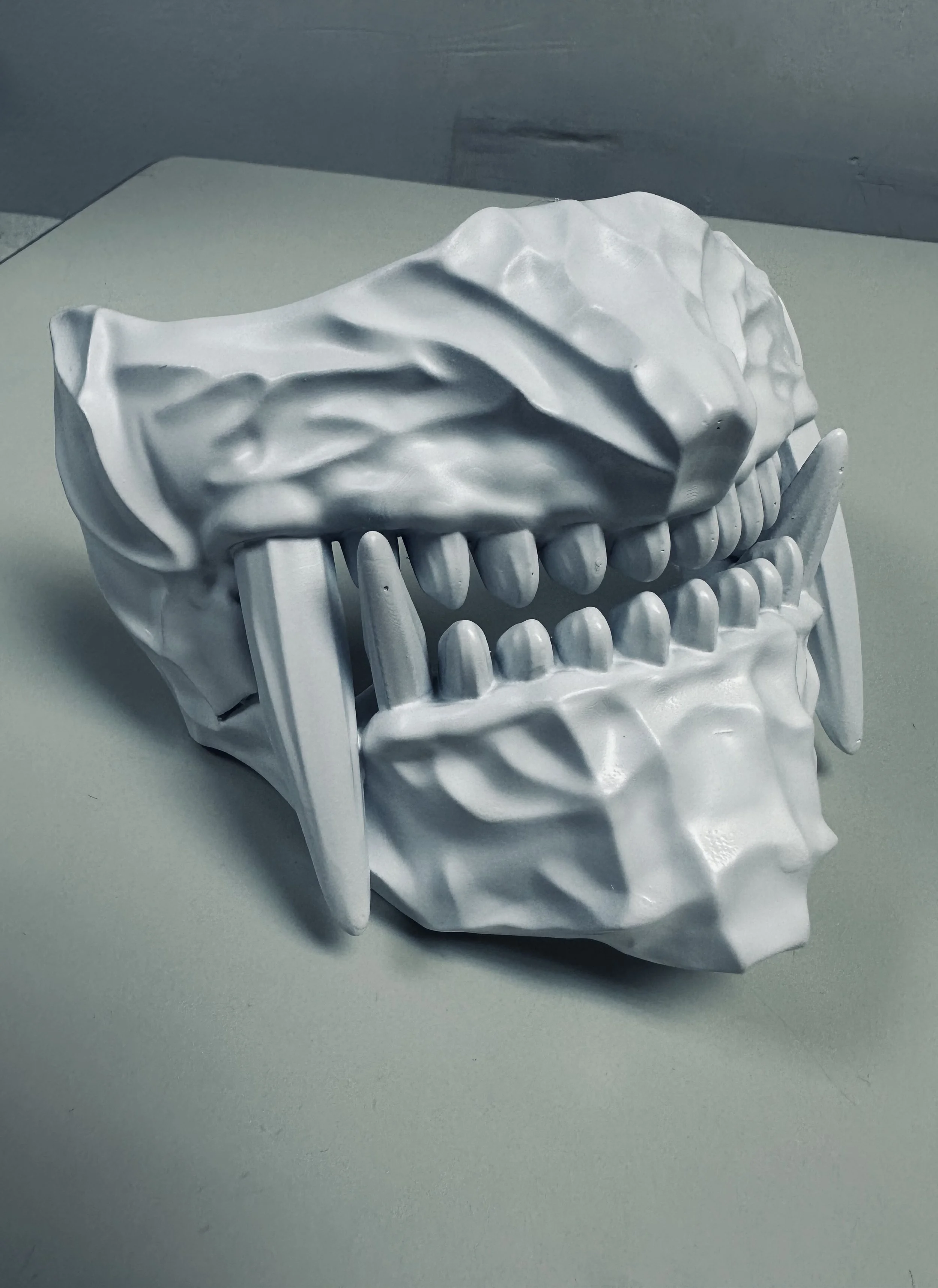 A white sculpture of a human skull with its jaw open, displaying teeth and exaggerated features.
