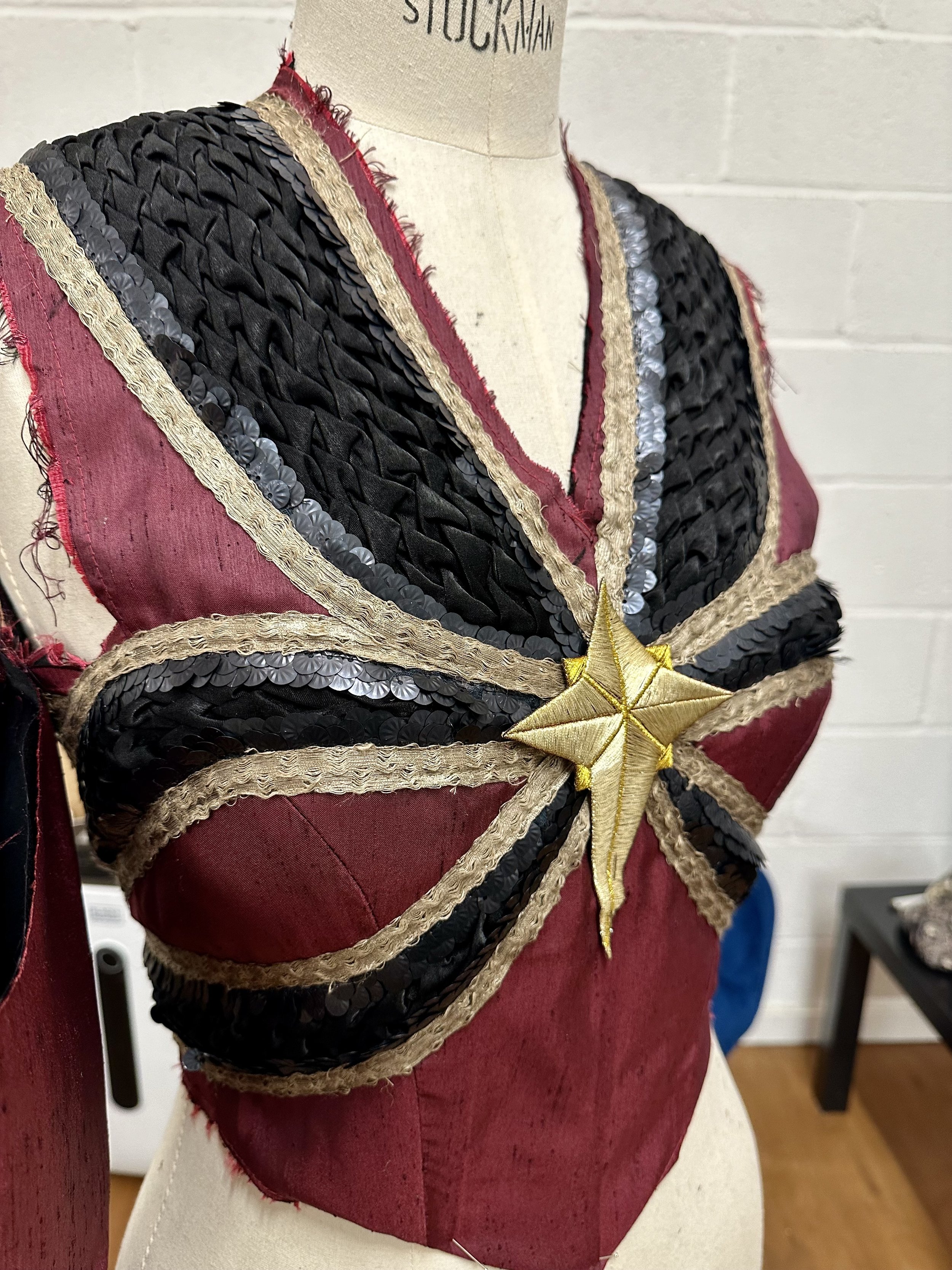 A decorative vest with black, gold, and red fabric along with sequins and a gold star embellishment in the center, displayed on a mannequin.