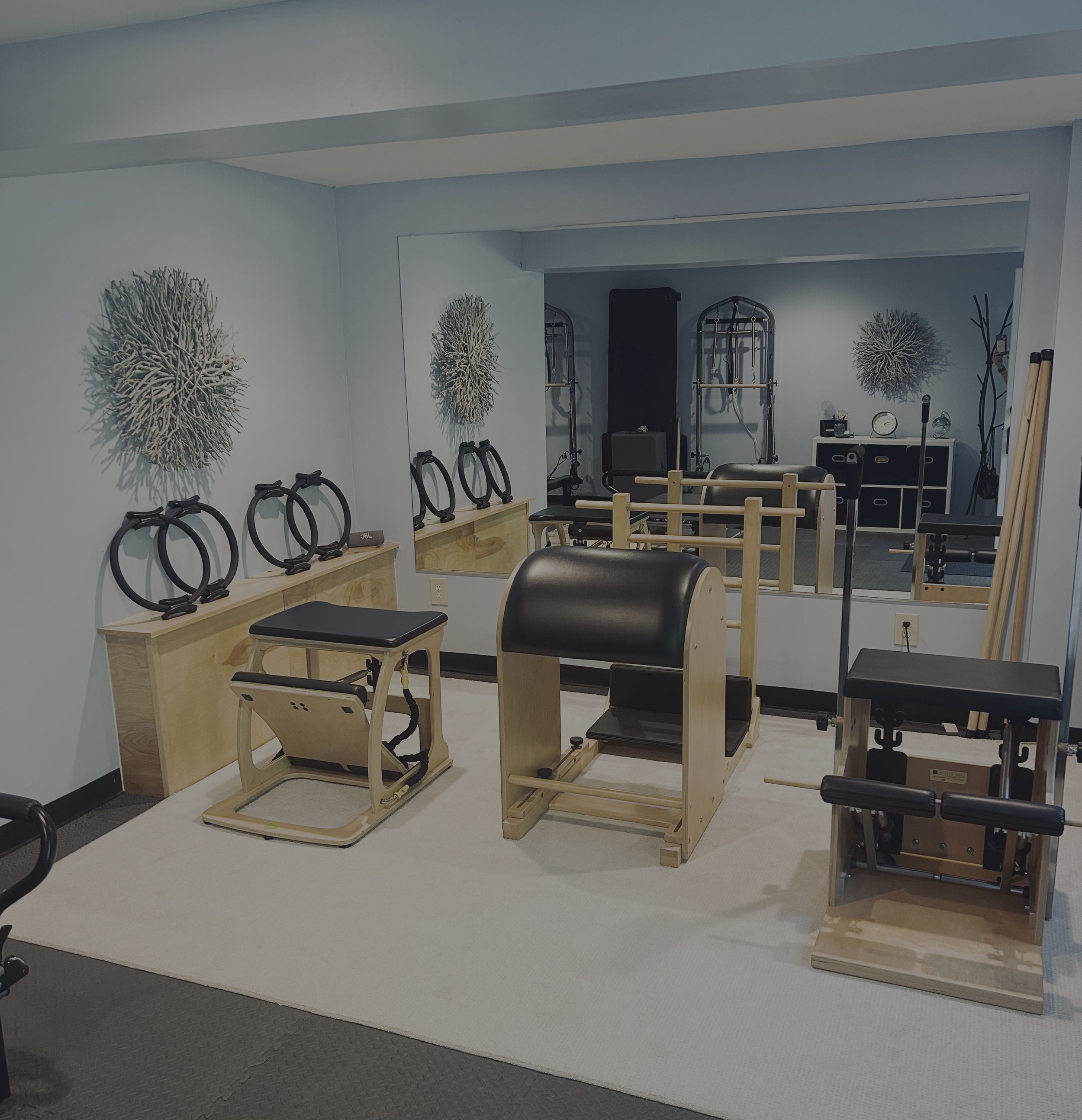 Pilates reformer machines and small exercise equipment in a well-lit fitness studio with wood-themed decor and a large mirror.