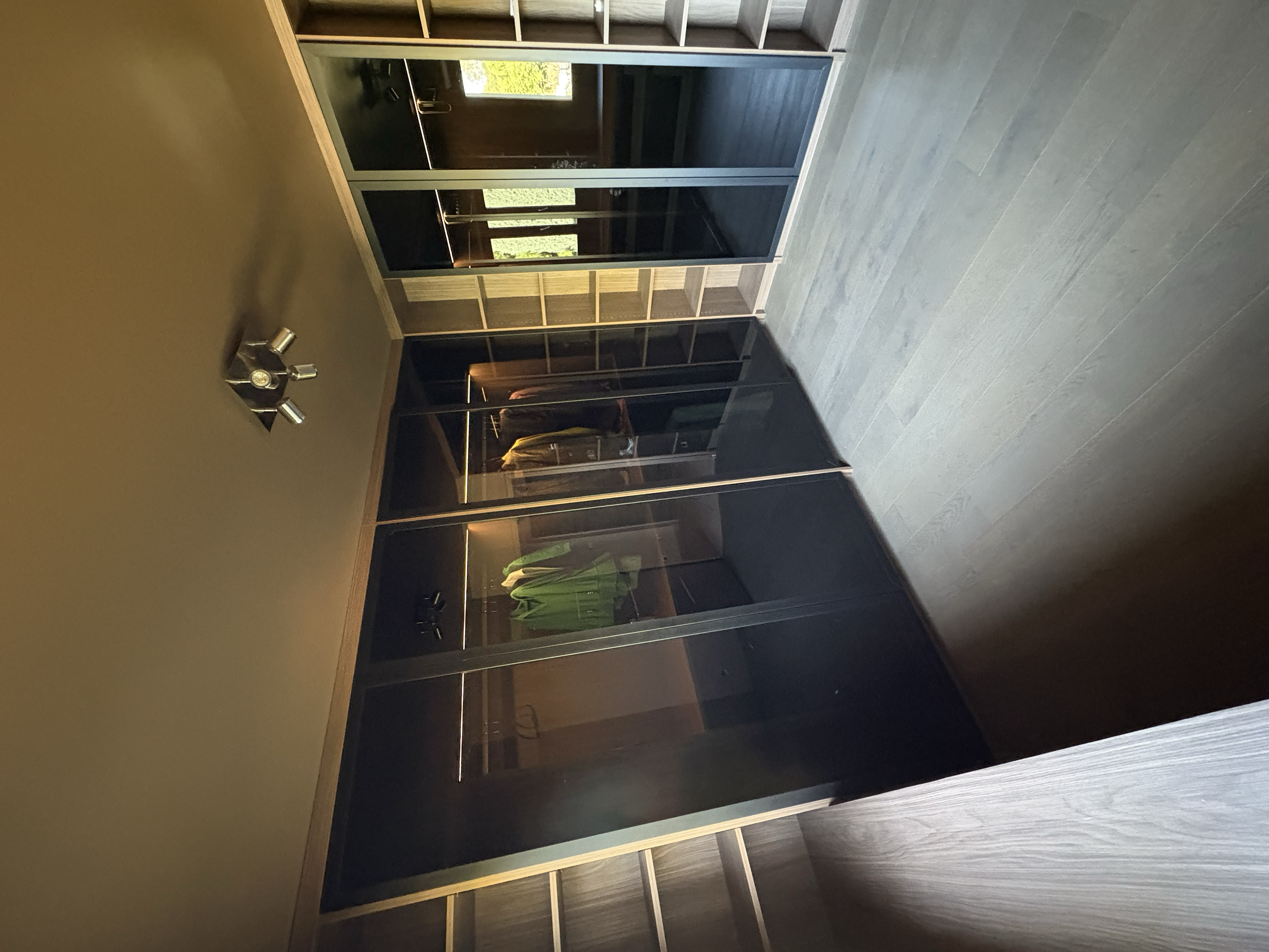 Garde-robe avec des portes en verre noir, située dans une pièce moderne avec un sol en bois clair et un mur beige.