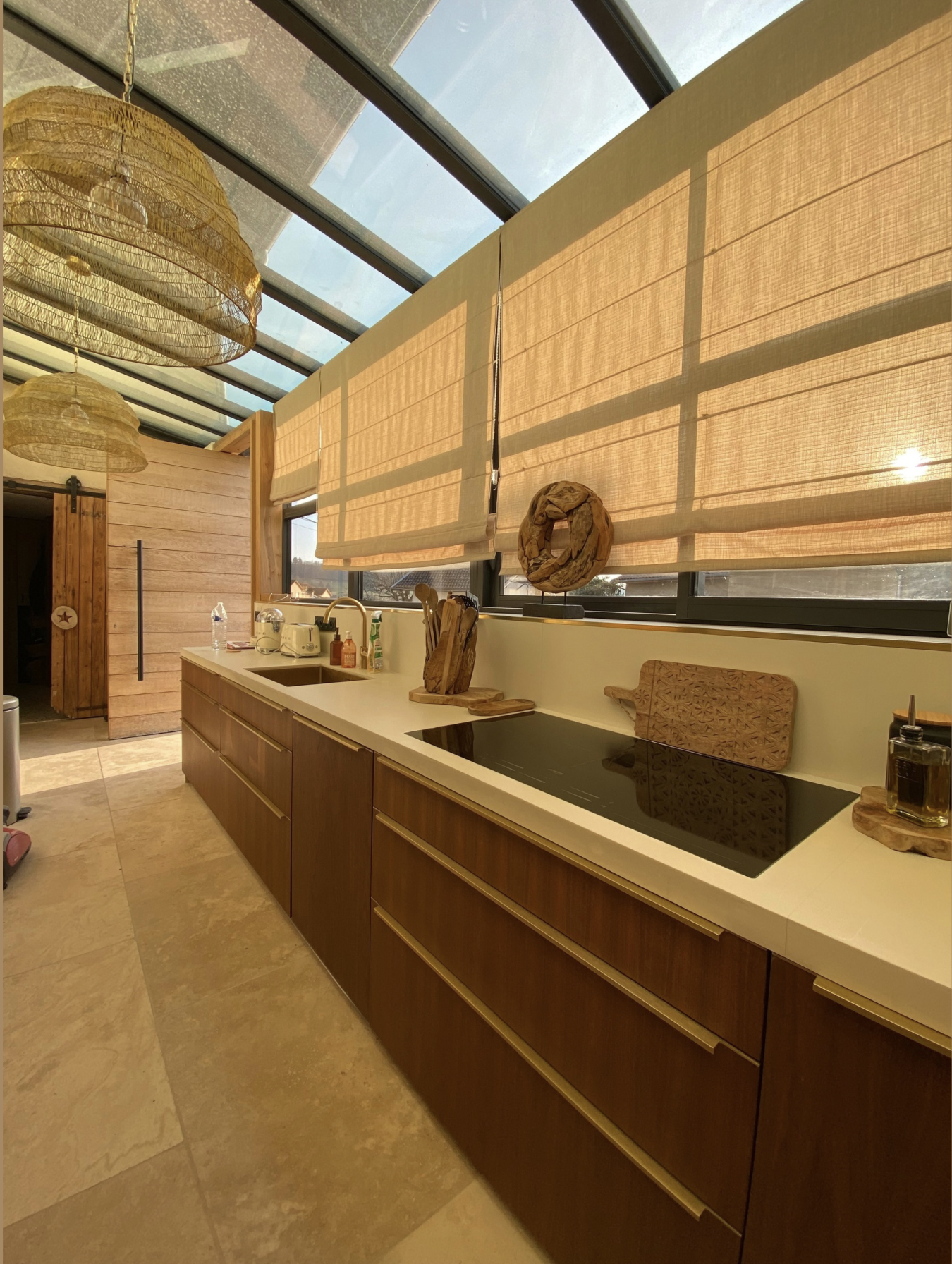 Cuisine moderne avec fenêtre en verre, comptoir en blanc, mobilier en bois foncé, éléments décoratifs en bois, appareils électroménagers, et rideaux en tissu beige.