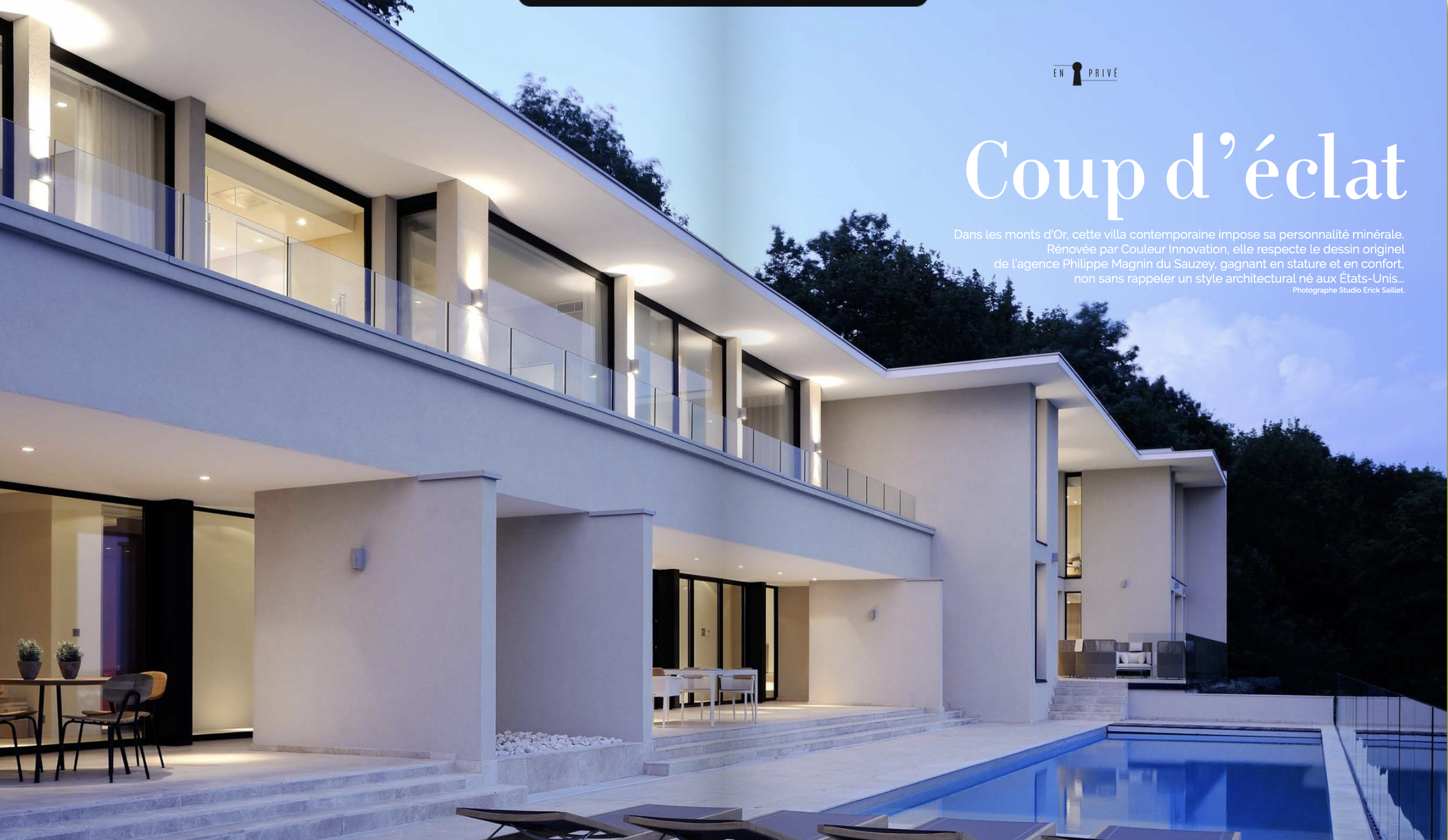 Une maison moderne avec une piscine extérieure illuminée la nuit, avec plusieurs étages, de grandes fenêtres et un balcon.