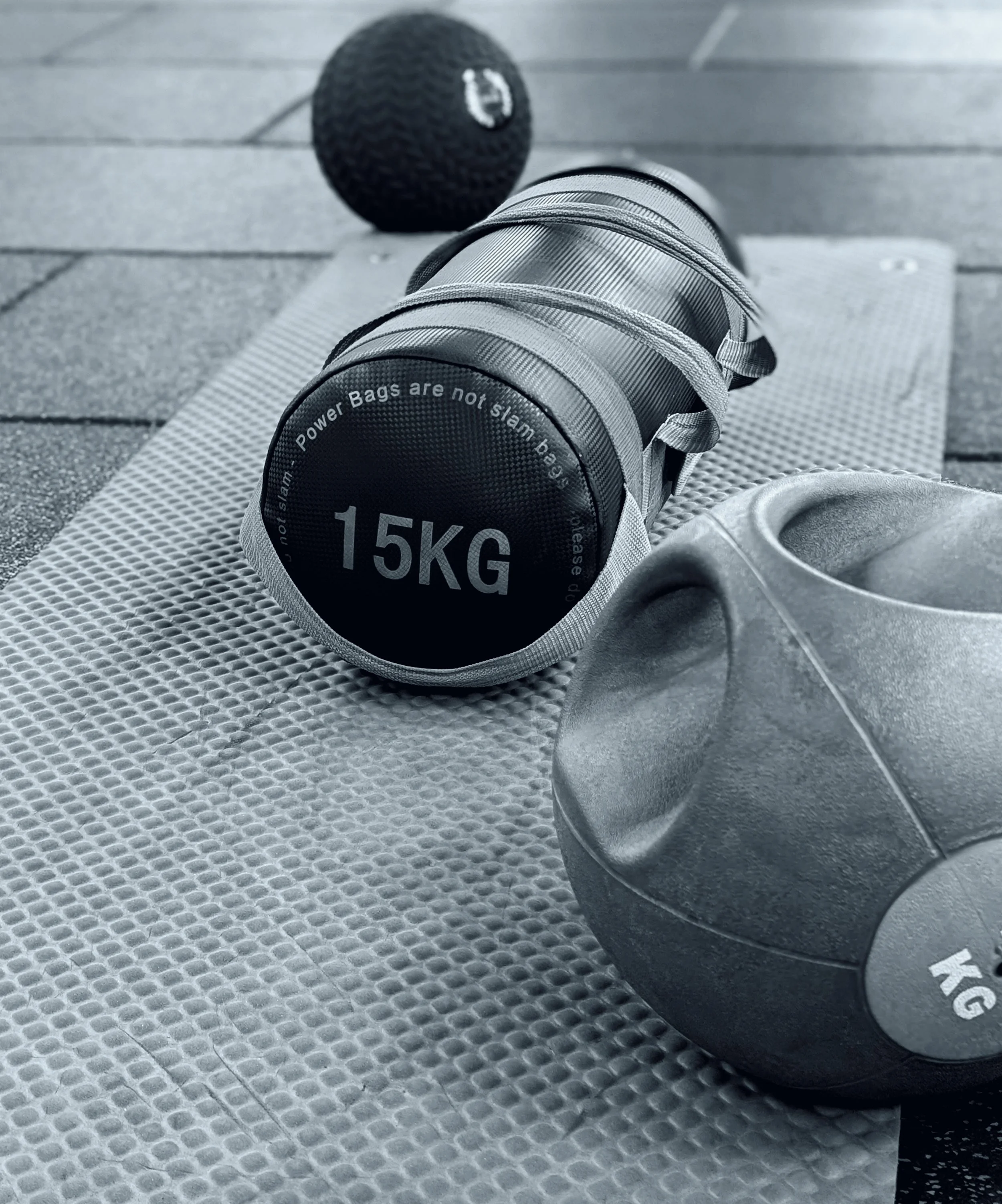 A personal training gym based in Chobham and Surrey. Close-up of a small exercise dumbbell with a weight label of 15KG, placed on a textured exercise mat, with a black foam roller in the background on a wooden floor.