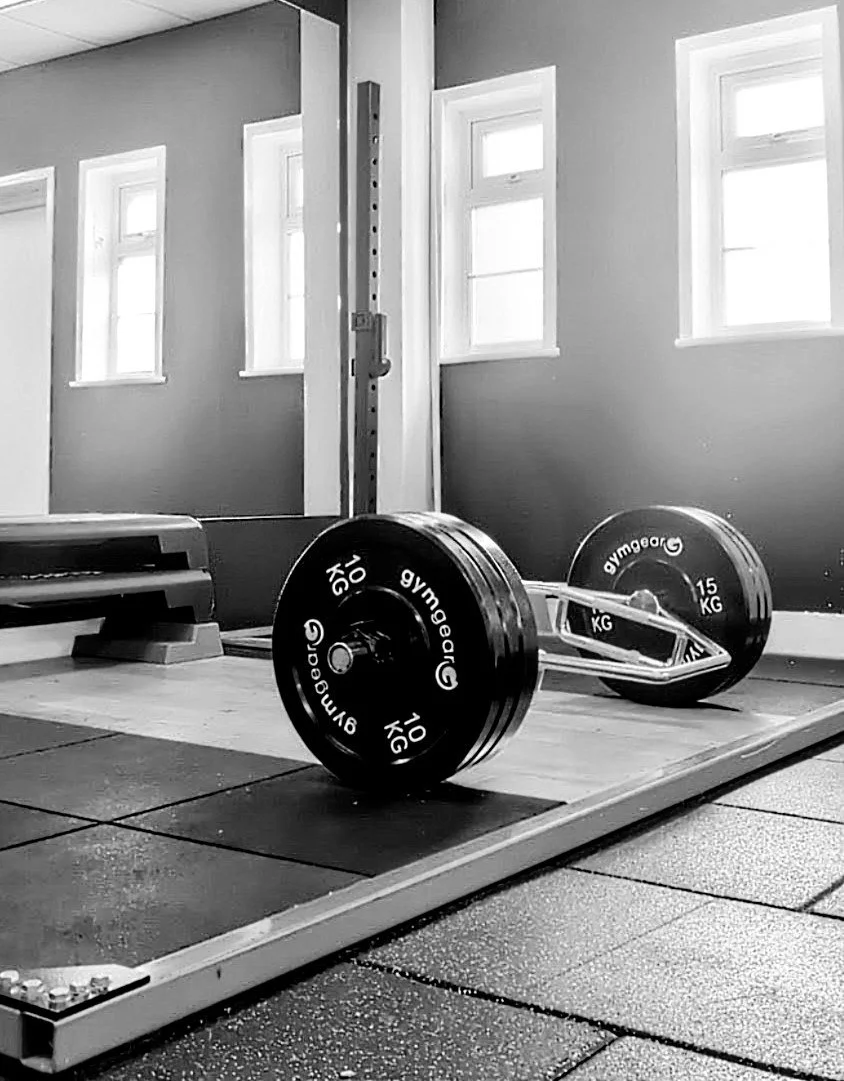 A personal training gym in Chobham and Surrey. A gym with a barbell loaded with weight plates on a lifting platform, near a mirror and windows.