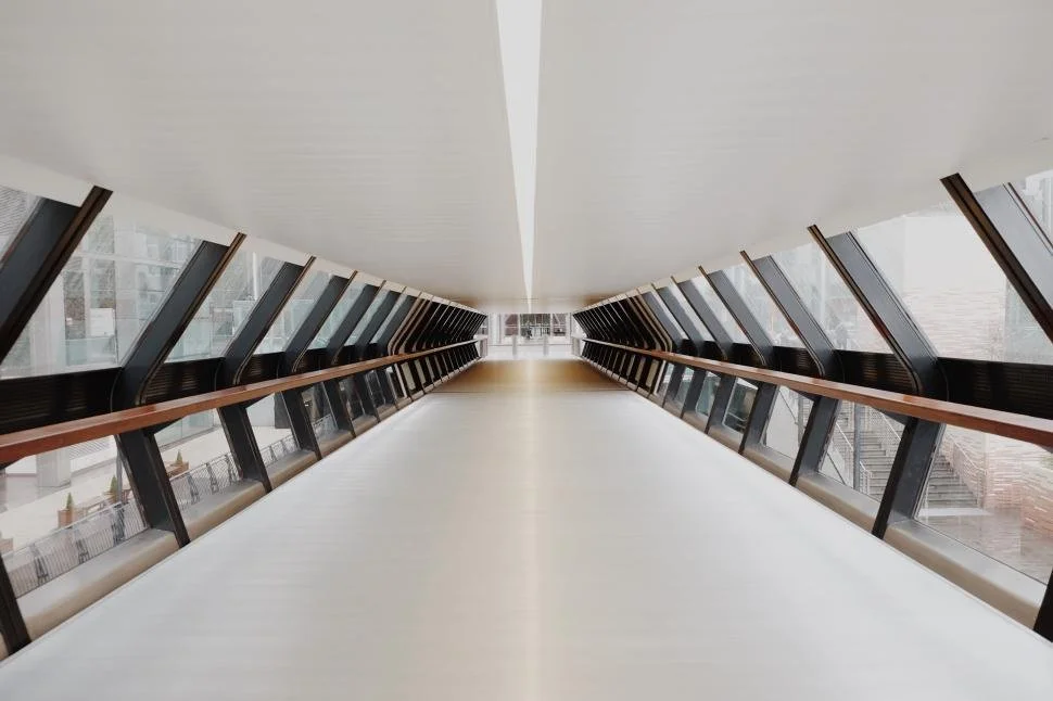Empty modern enclosed pedestrian bridge with glass windows and wooden handrails.