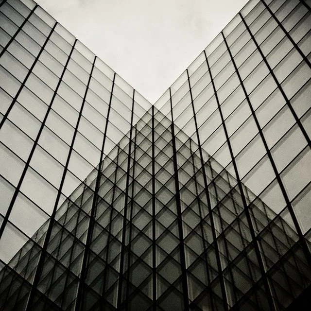 View of modern glass building with geometric lines and reflective windows, taken from a low angle upwards.