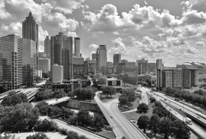 Black and white photo of a city skyline with tall skyscrapers and highway interchange with moving vehicles.