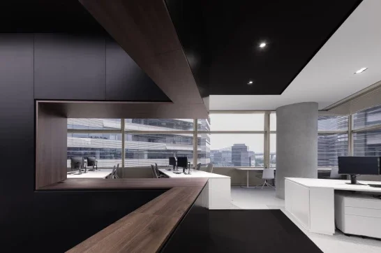 Modern office interior with large windows, desks, and office chairs, featuring a combination of dark and white furniture and a cityscape view outside.