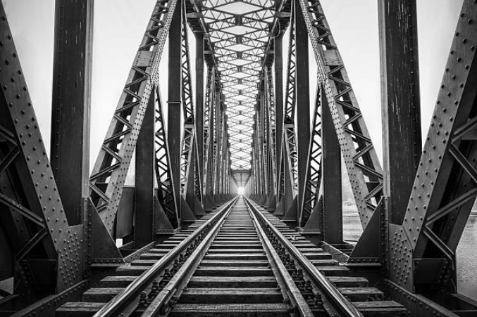 Black and white photo of a railway bridge with metal trusses and tracks leading into the distance