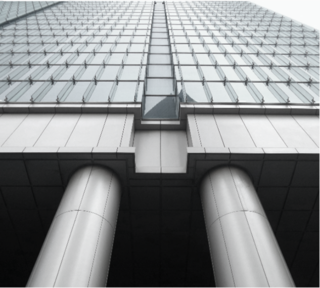 Low-angle view of a modern glass skyscraper with two large cylindrical support columns at the base.