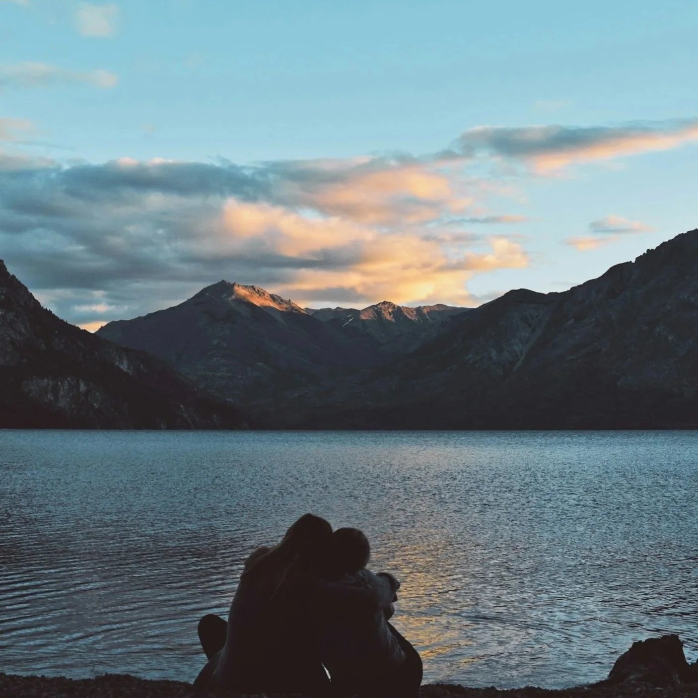 Two people embracing by a mountain lake, representing connection and support