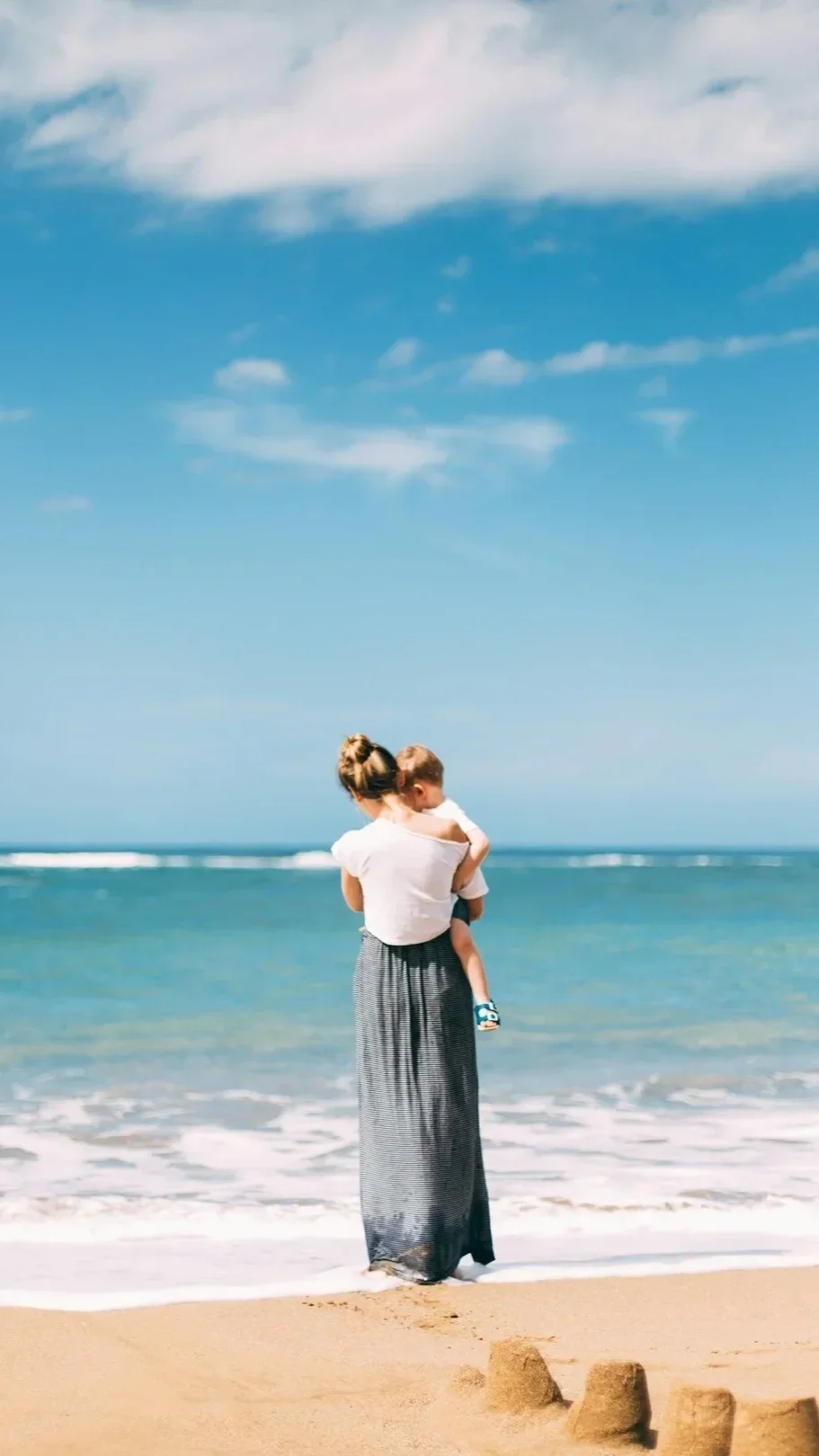 Mother carrying her child by the ocean, symbolizing connection, motherhood, healing, and parenting support.