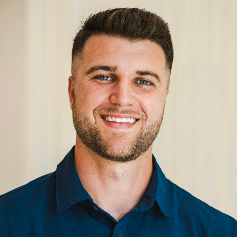 A young man with short brown hair, blue eyes, and a beard, smiling and wearing a dark blue collared shirt.