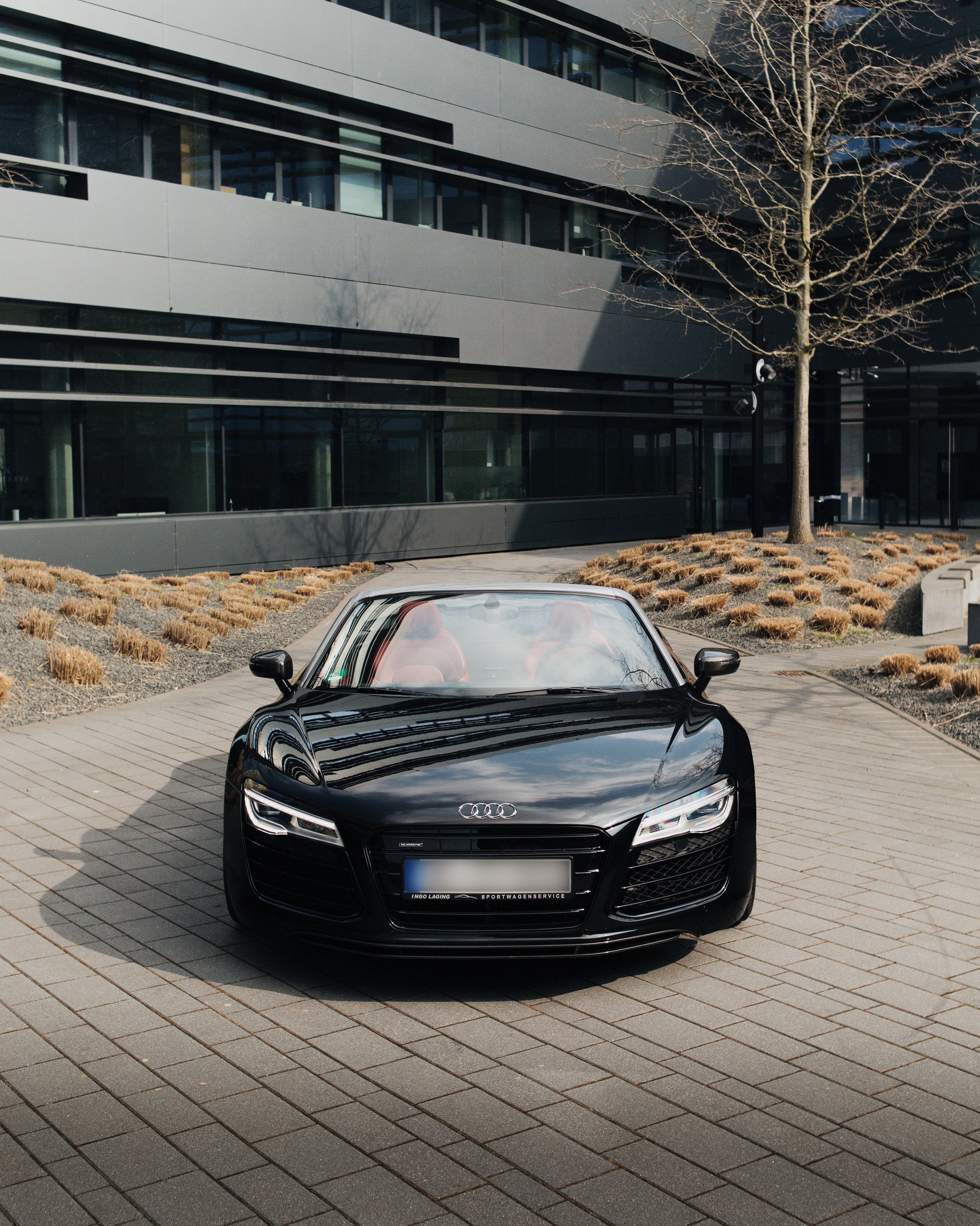 Schwarzer Audi Sportwagen parked vor modernem Bürogebäude mit Bäumen und Pflanzbeeten