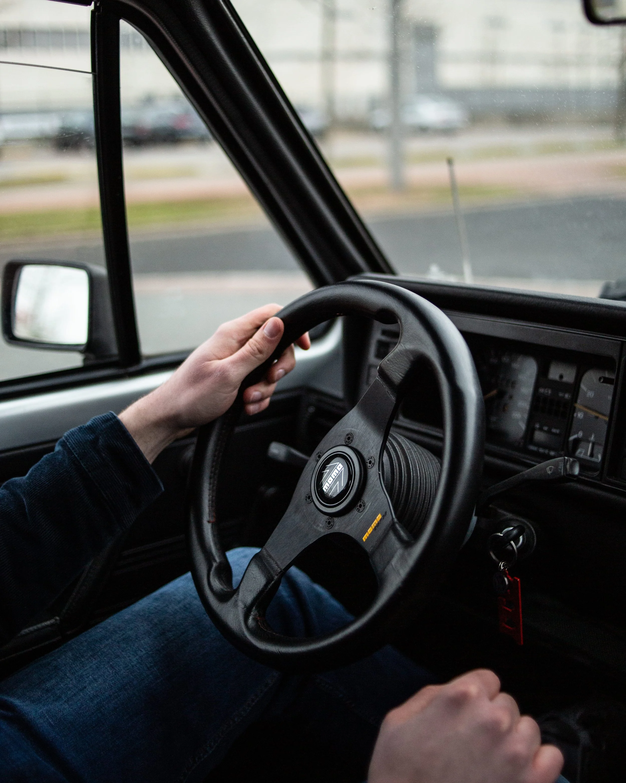 Innenansicht eines Fahrzeugs mit einer Hand auf dem Lenkrad und einem Schaltknüppel, Blick auf die Straße durch die Windschutzscheibe.