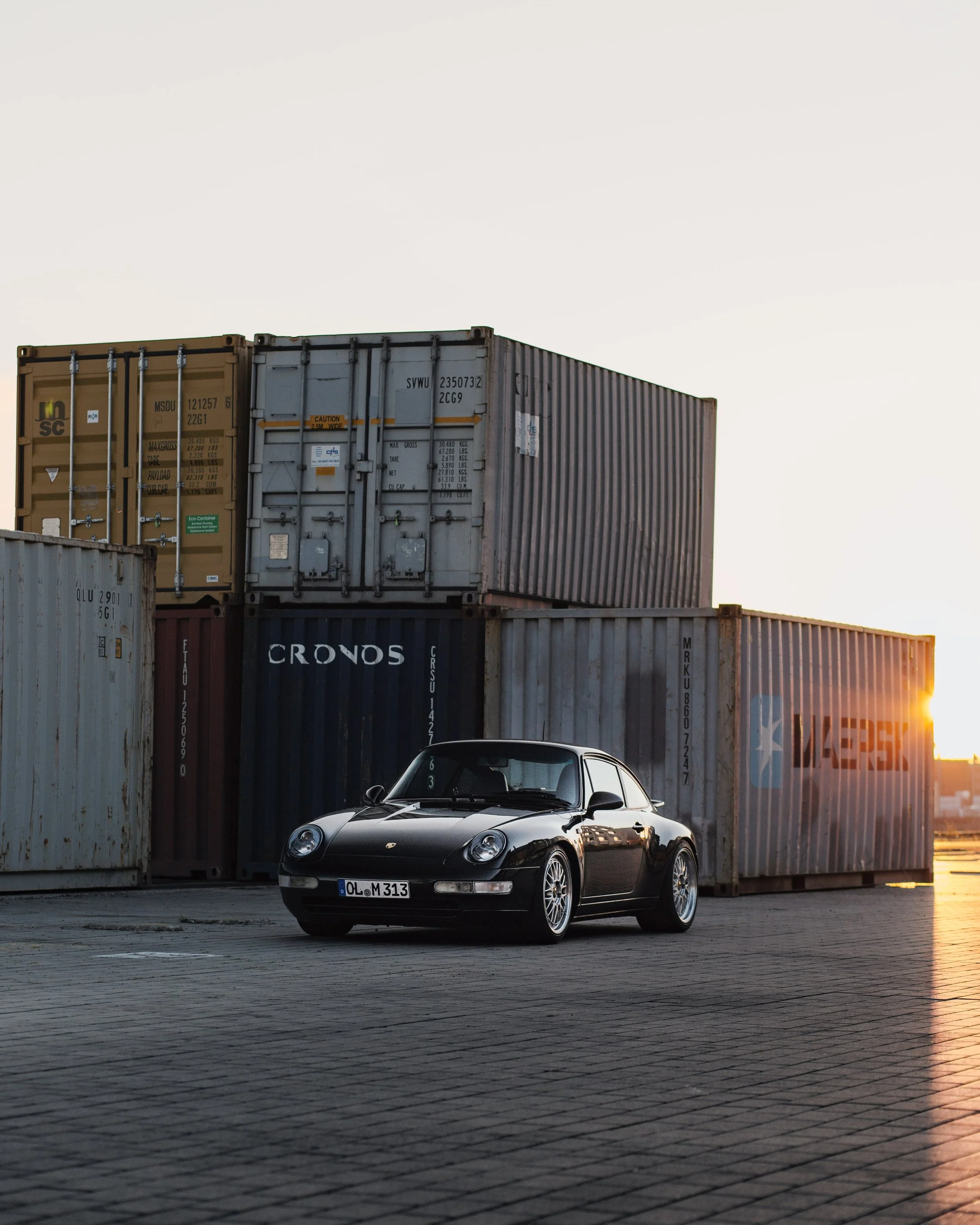 Schwarzer Porsche 911 vor Container im Sonnenuntergang.