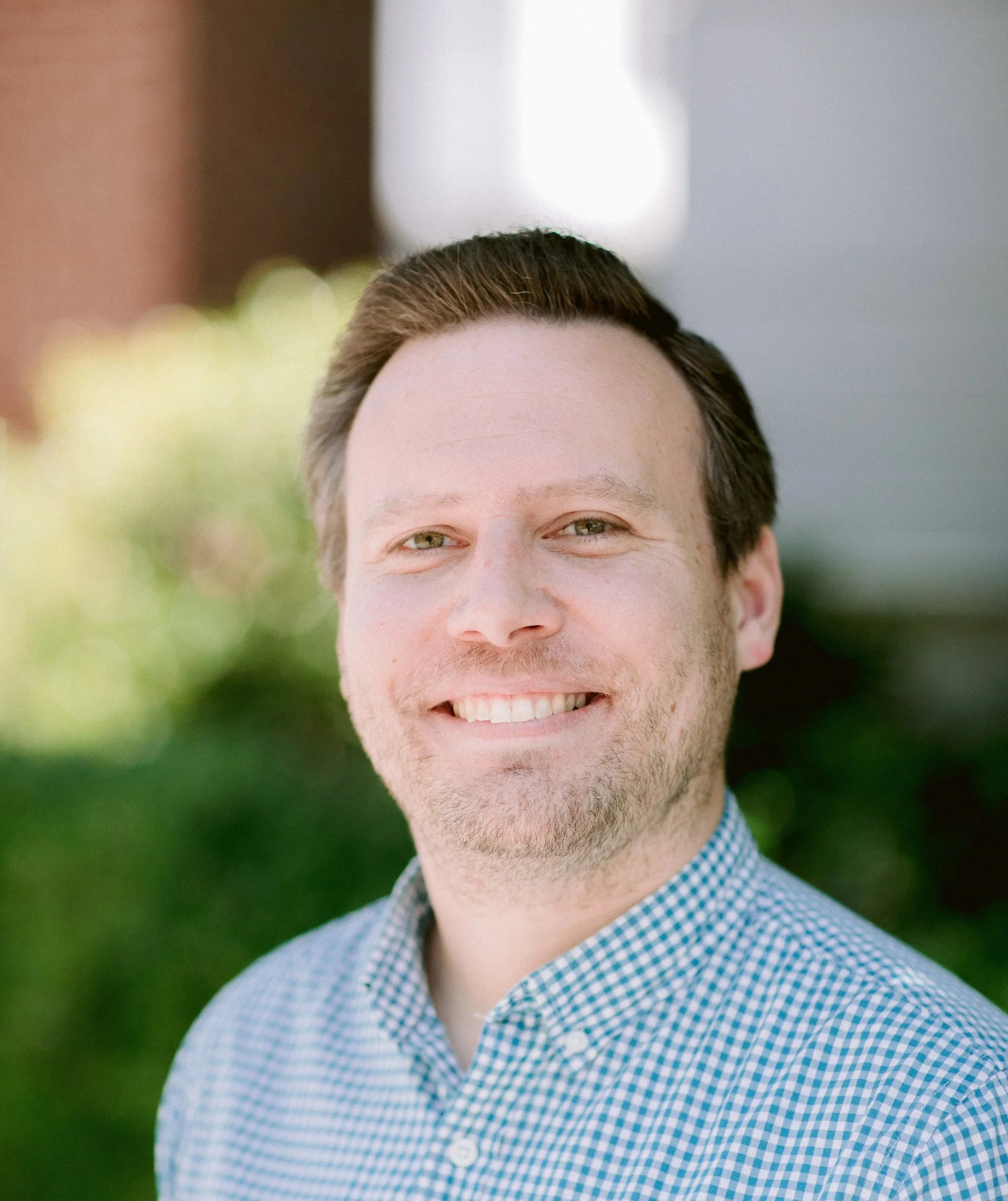 Portrait of a smiling man with light skin, light brown hair, and wearing a blue checkered shirt