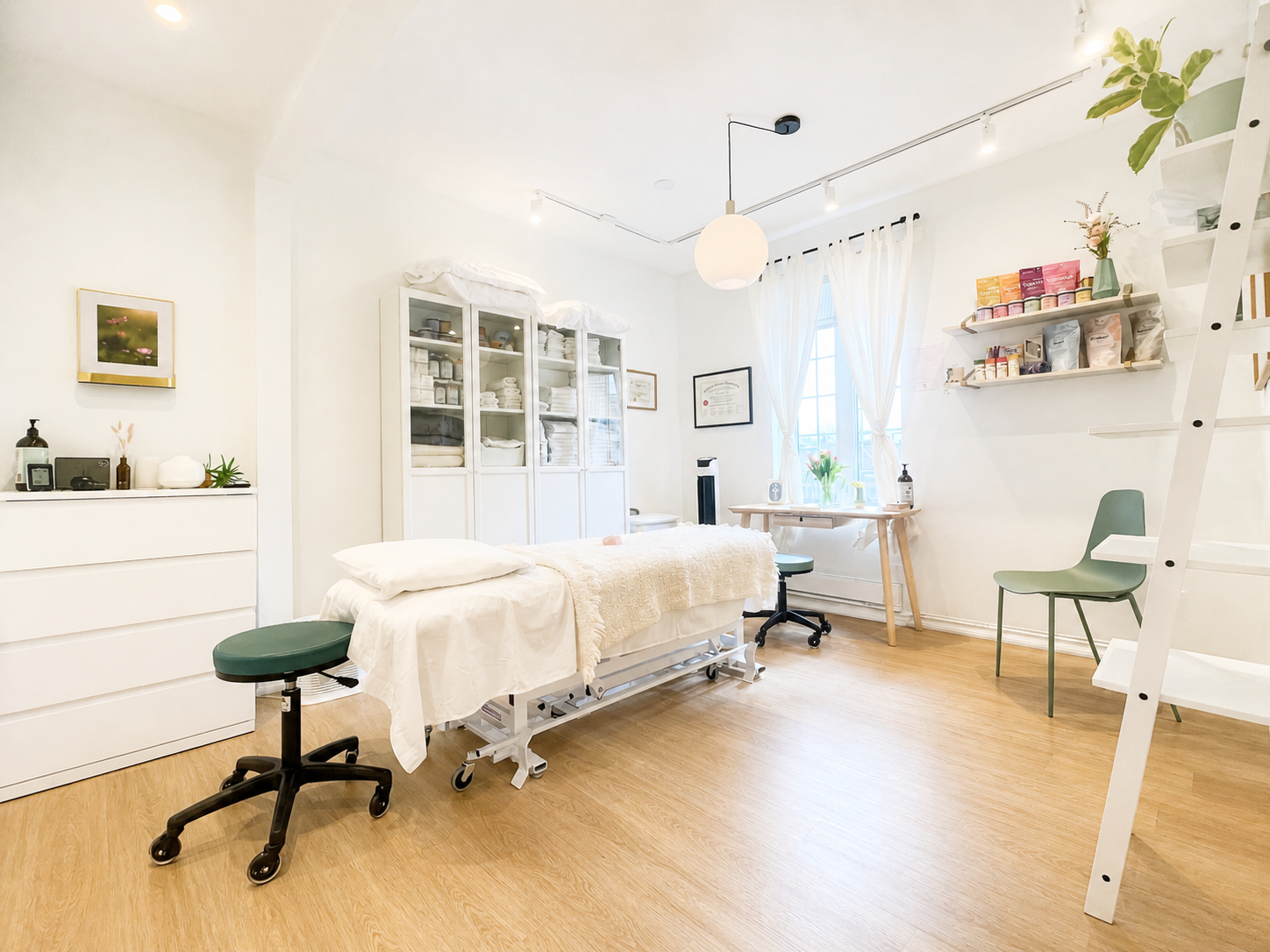 Medical treatment room with a bed, green stools, white cabinets with linens, wall shelves with products, a green chair, a window with curtains, and a ladder leading to a loft space.