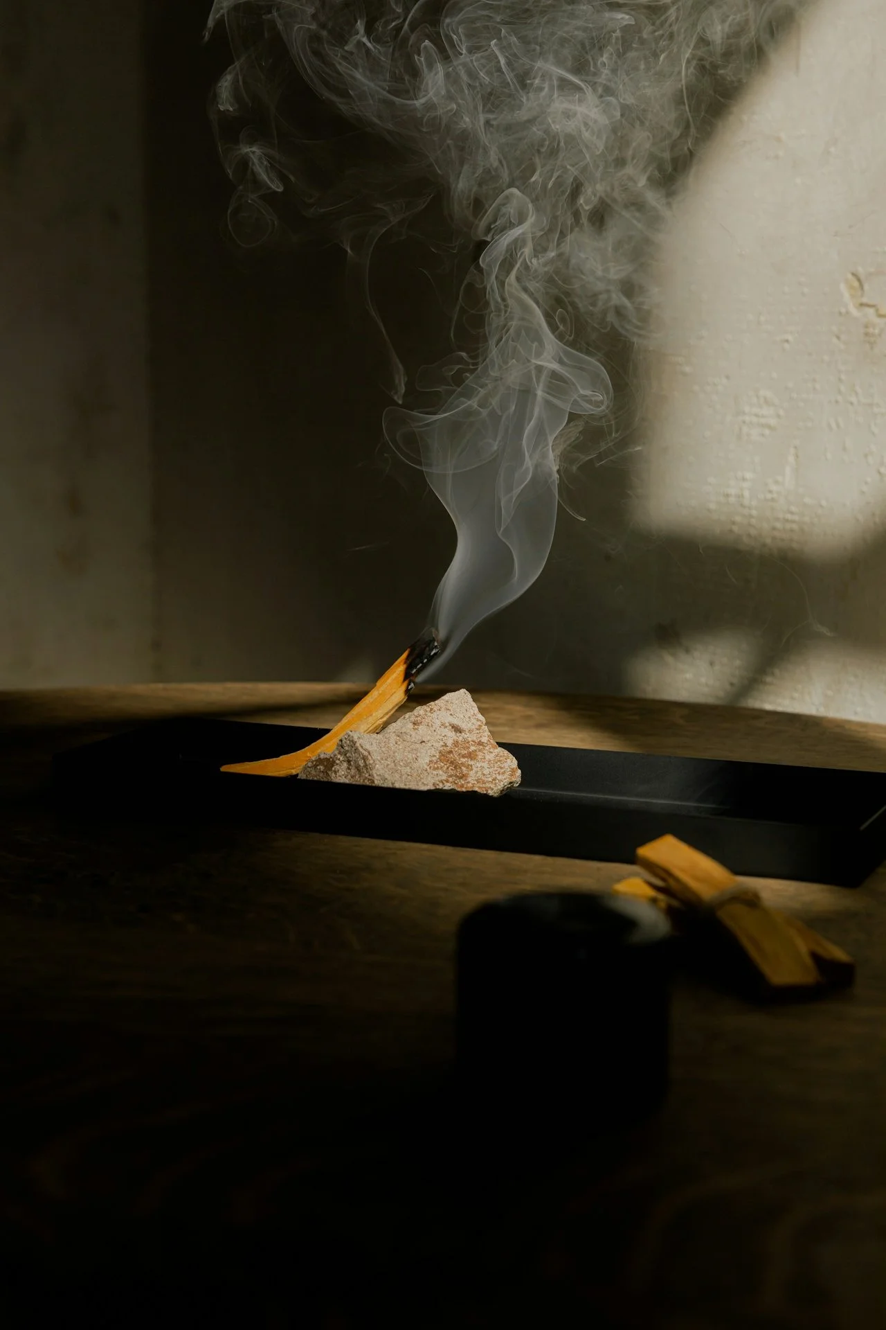 Incense stick burning on a rock, smoke curling upwards in a dimly lit setting.