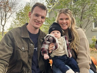 A family of three outdoors, with the man and woman smiling and holding a baby.