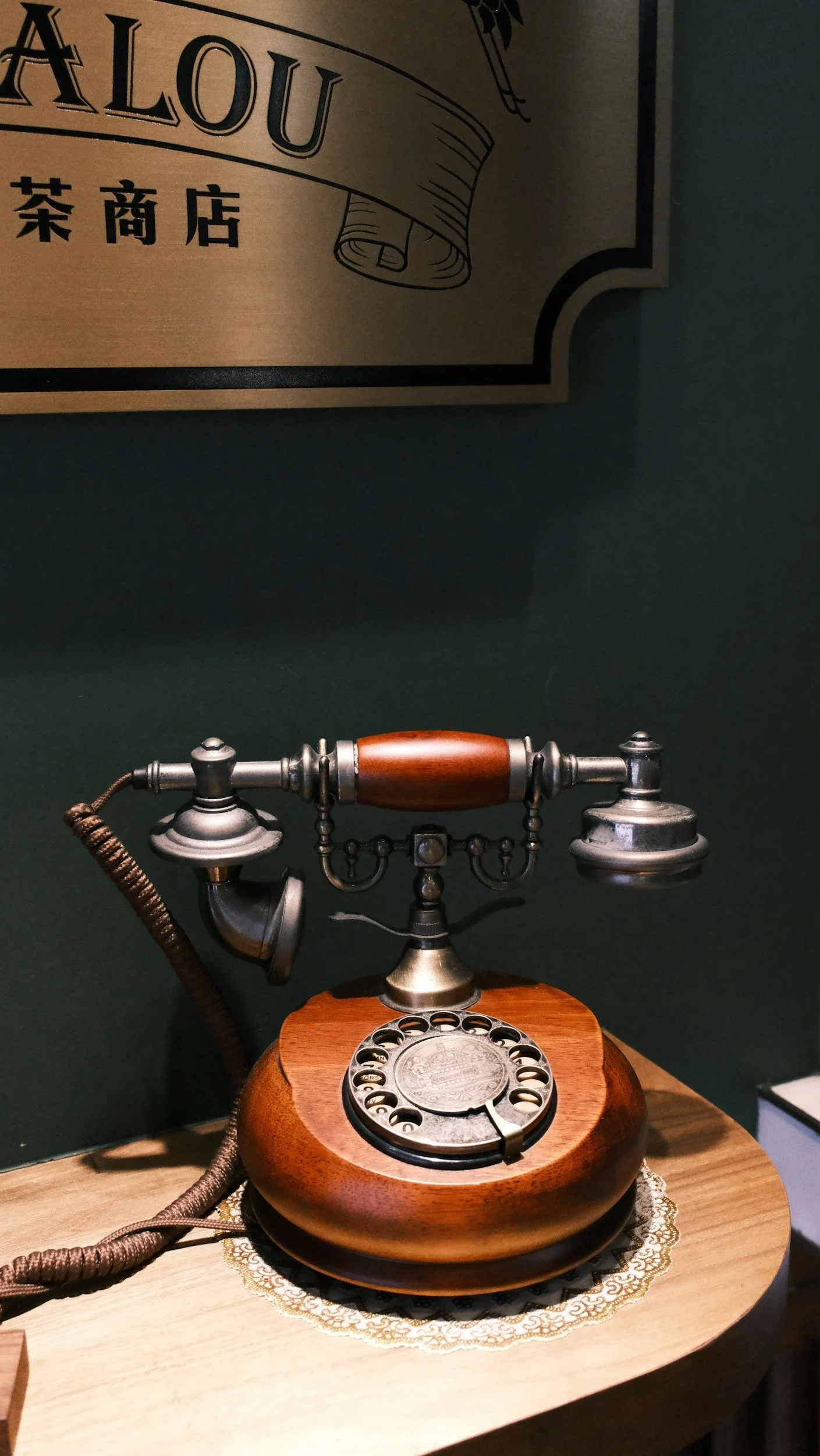 Vintage rotary telephone with wooden base and metal components displayed on a table.