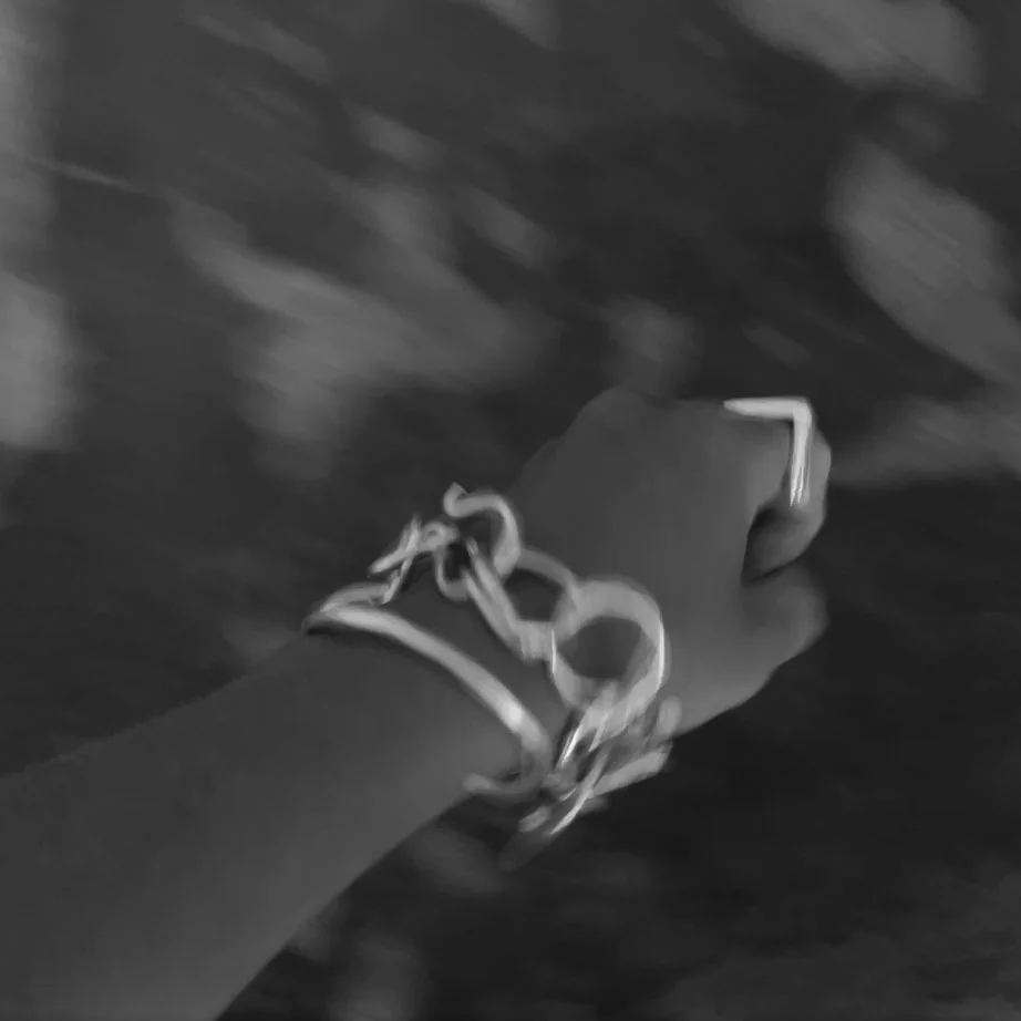 A person wearing a bracelet, holding an object, walking on a textured ground.