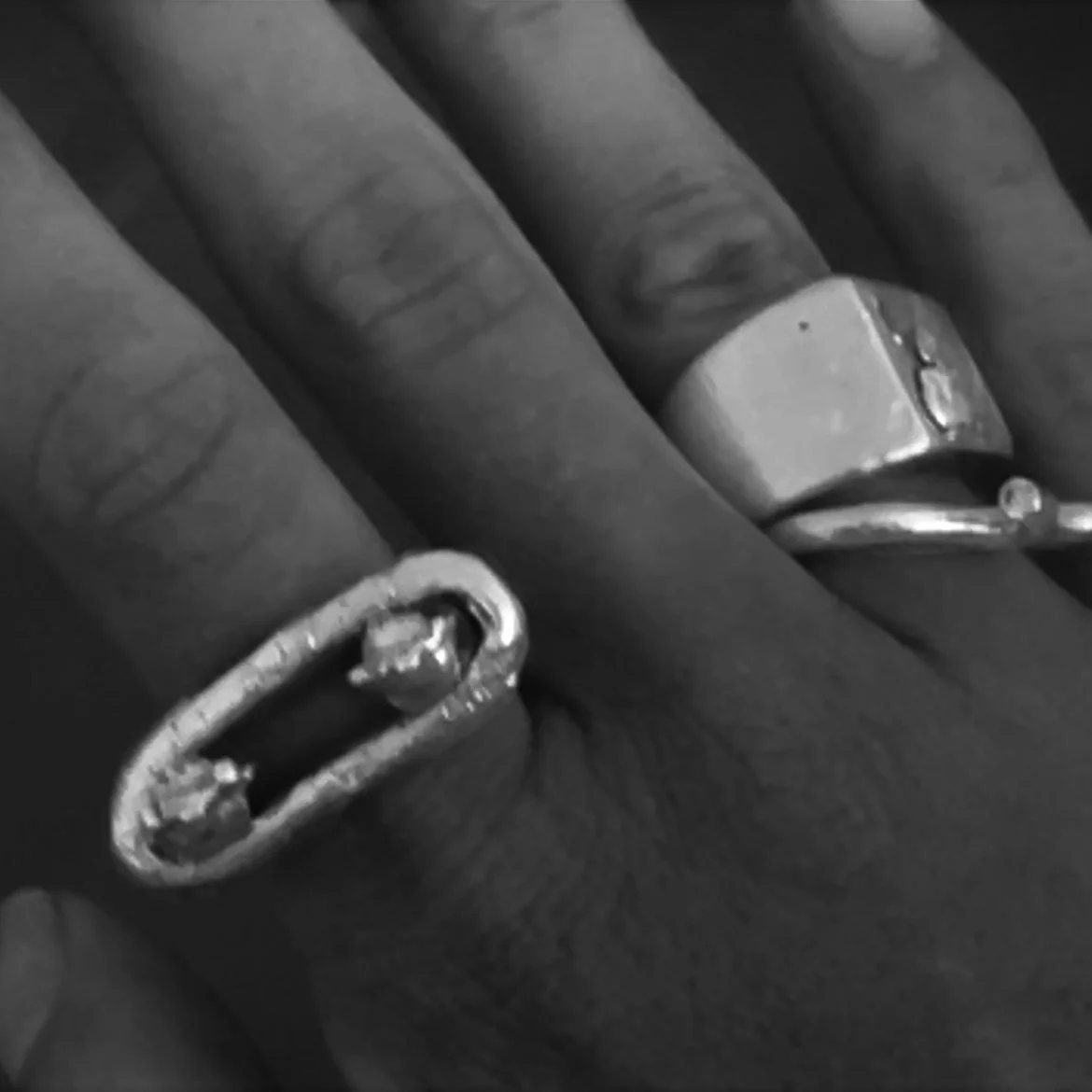 Close-up of a hand wearing two rings, one on the middle finger and one on the ring finger, in black and white.