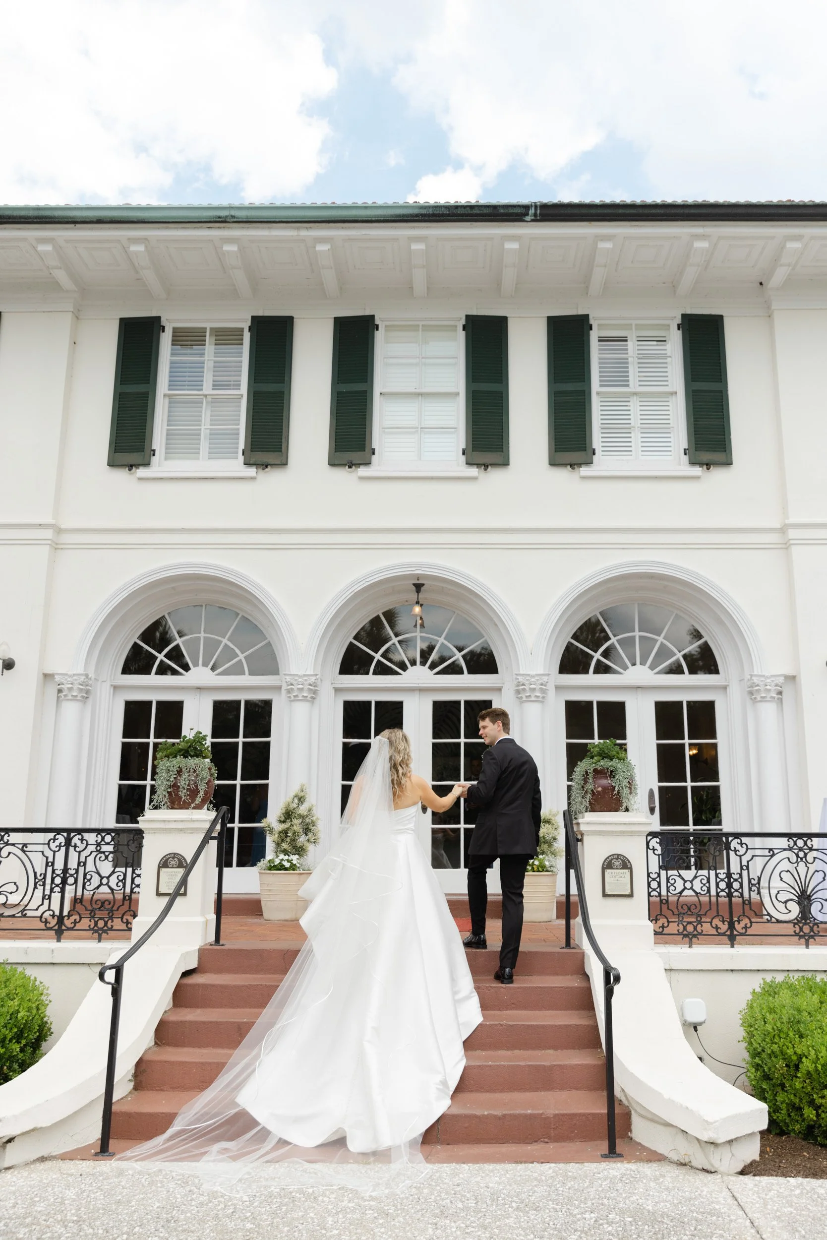 Bride and groom holding hands as they walk the steps of Cherokee Cottage at Jekyll Island Club in Georgia.
