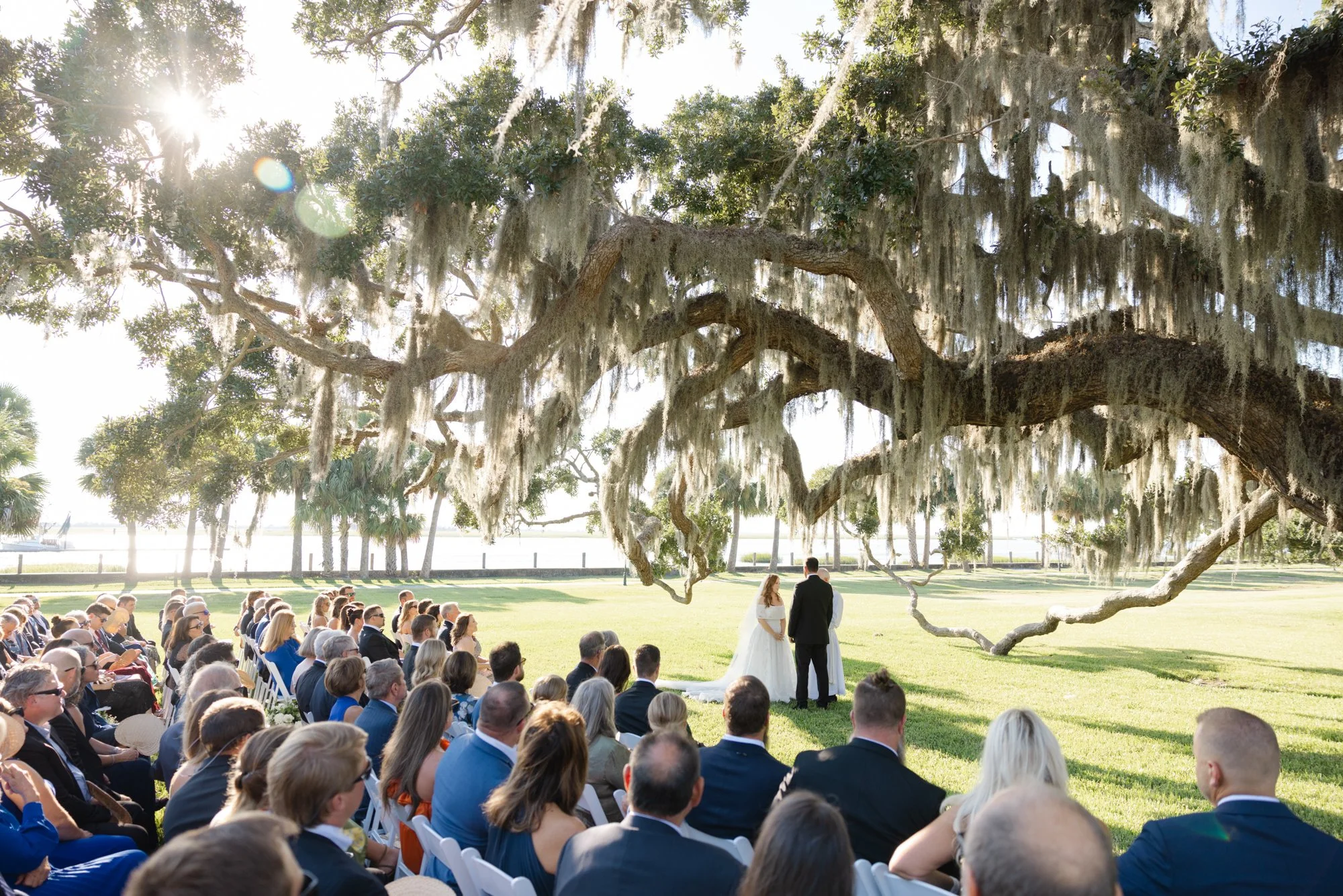Bride and groom standing beneath a sweeping live oak with hanging moss during their wedding ceremony on the Riverfront Lawn at Jekyll Island Club.