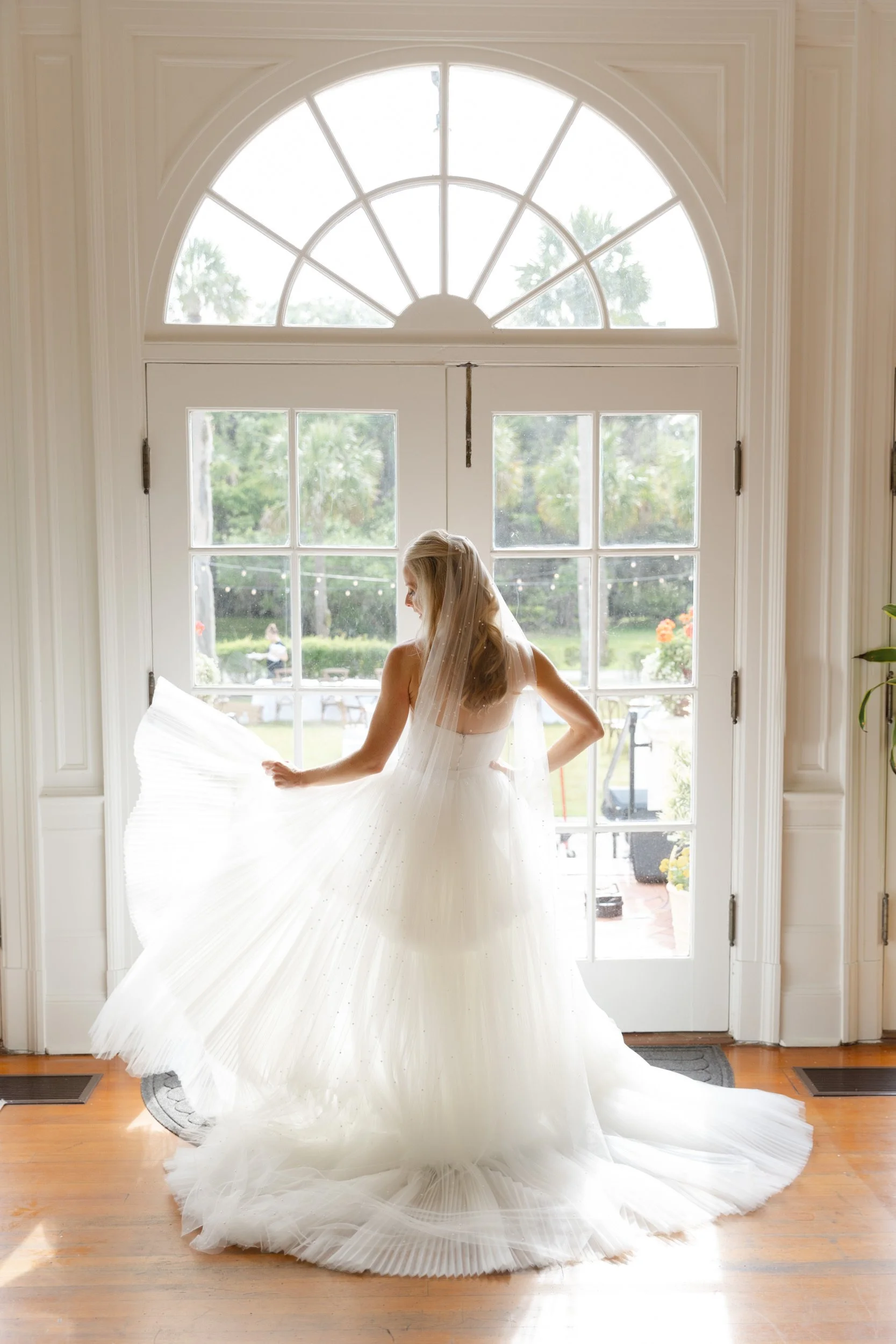 Fashion forward bride striking an editorial pose while swishing her dress in front of the glass doors at Cherokee Cottage on Jekyll Island, Georgia.