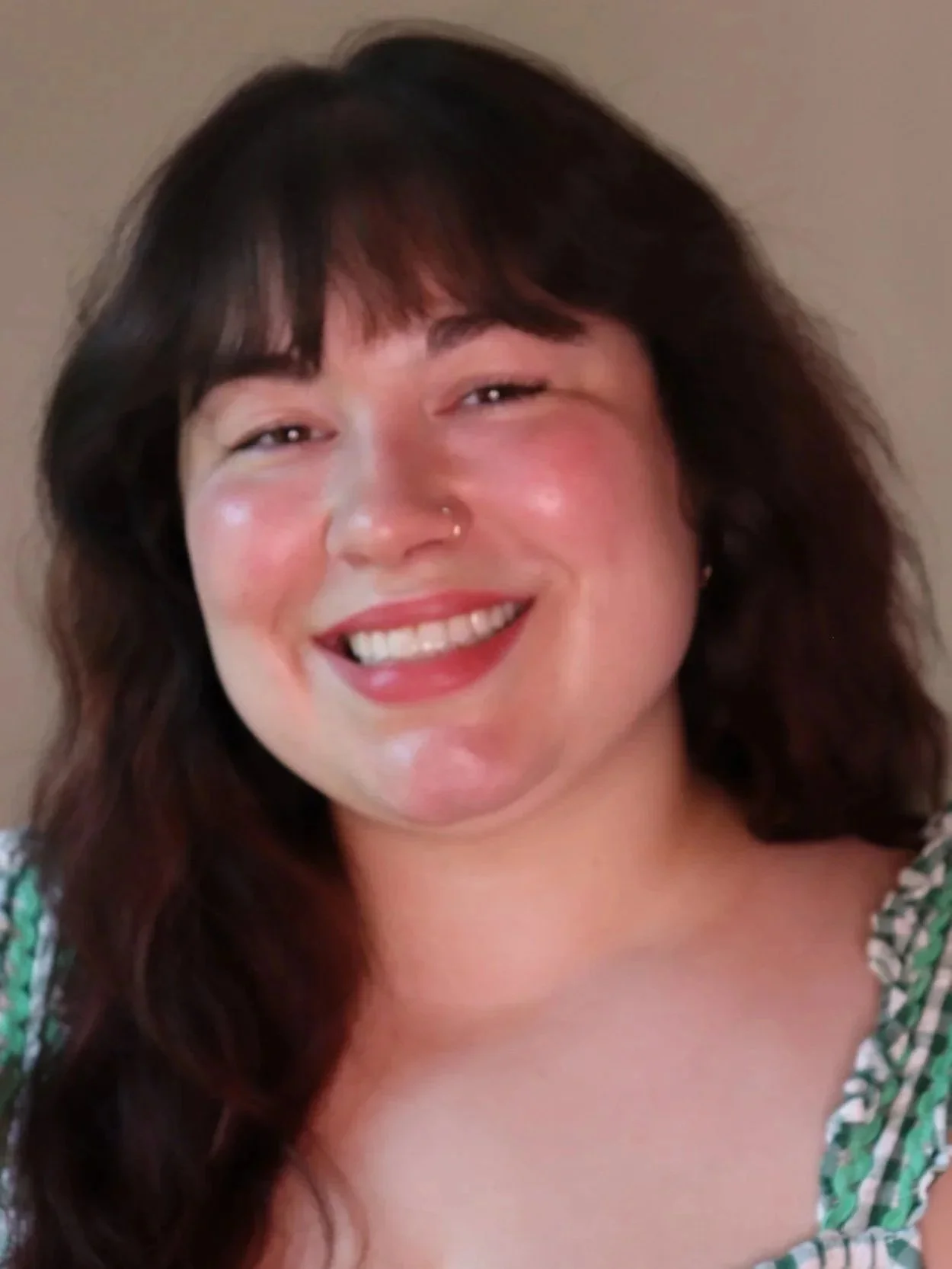 Close-up of a smiling woman with medium-length dark brown hair and wearing a green patterned top.