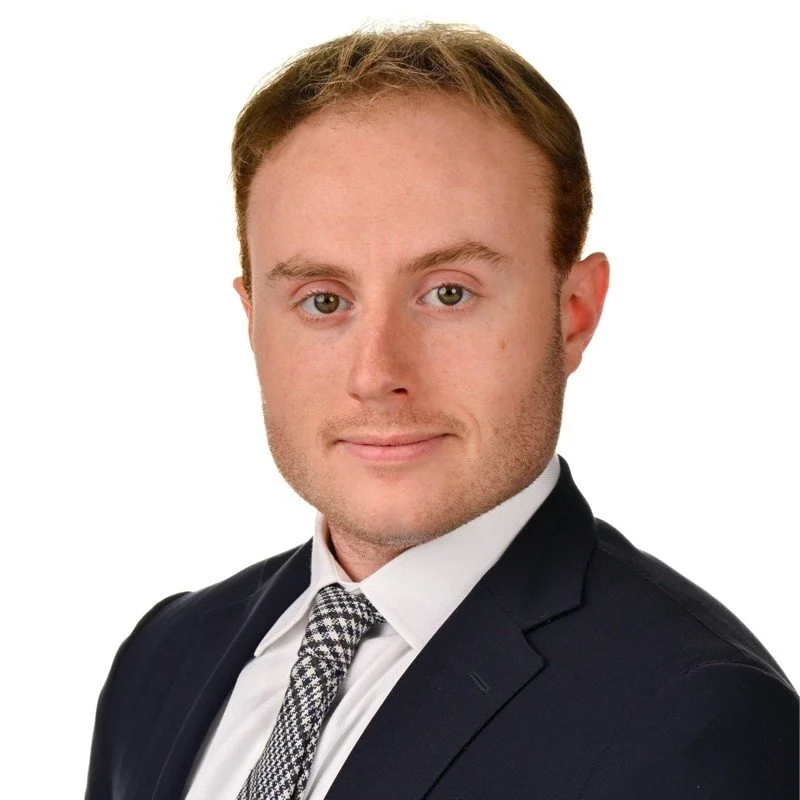 Professional headshot of a young man in a dark suit, white shirt, and patterned tie against a white background.