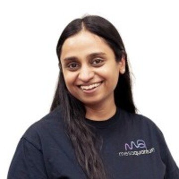 Smiling woman with long dark hair wearing a black shirt with a logo, against a white background.