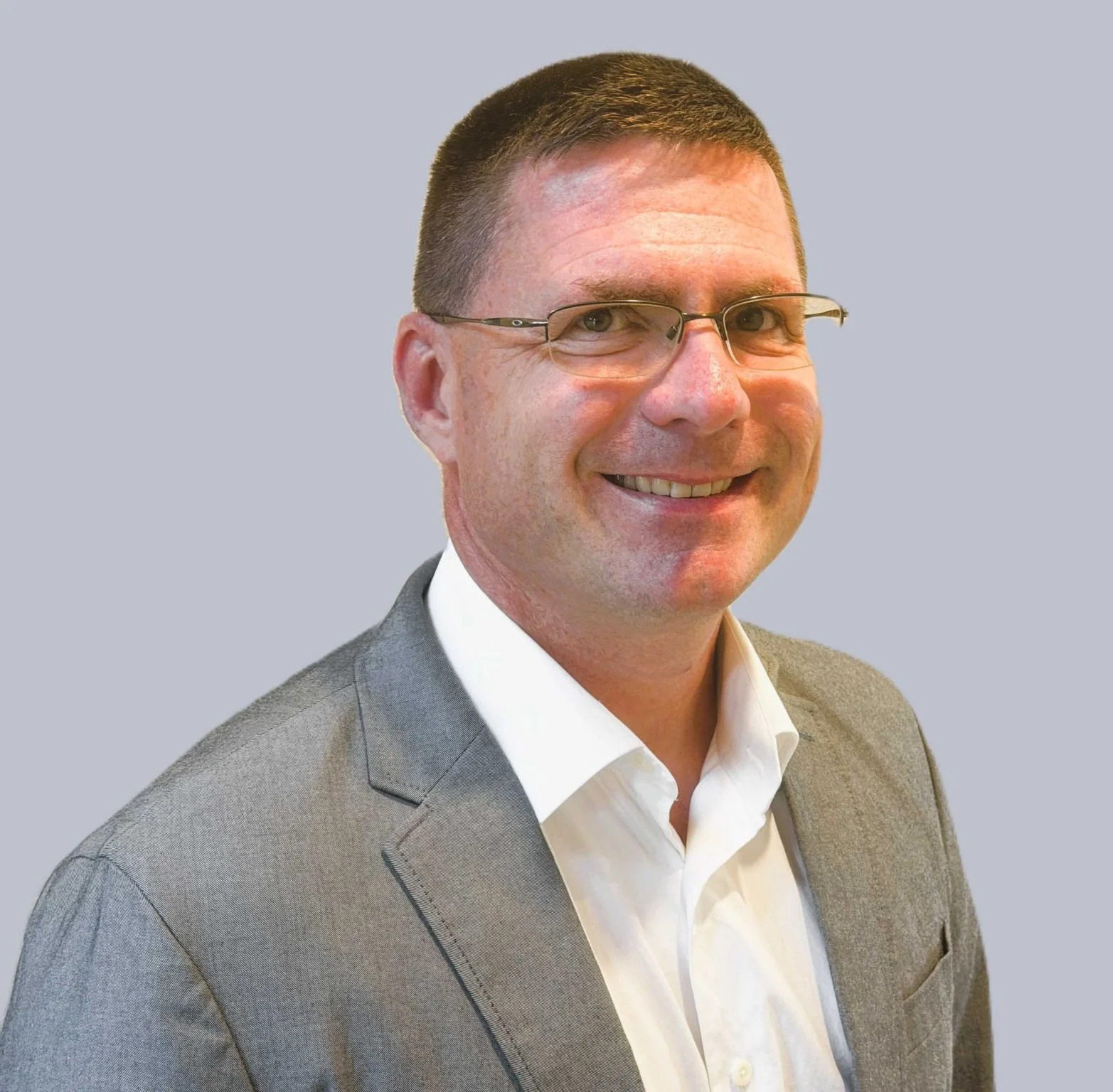 Man in grey suit jacket and white shirt, wearing glasses, smiling at the camera.