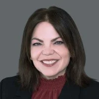 Portrait of a woman with shoulder-length dark hair, smiling, wearing a black blazer and red top.
