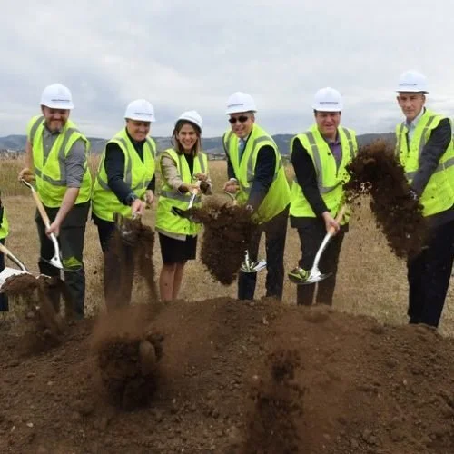 Group of seven people in safety vests and helmets planting a tree in an open field.